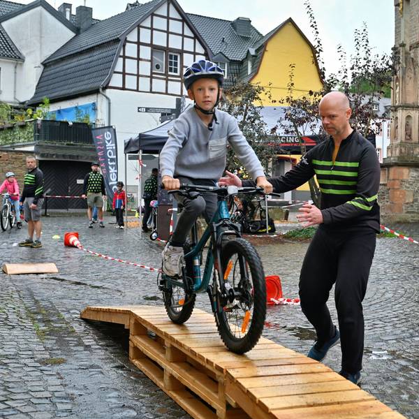 Ein Junge fährt mit dem Fahrrad über eine hölzerne Rampe, ein Mann gibt Hilfestellung.