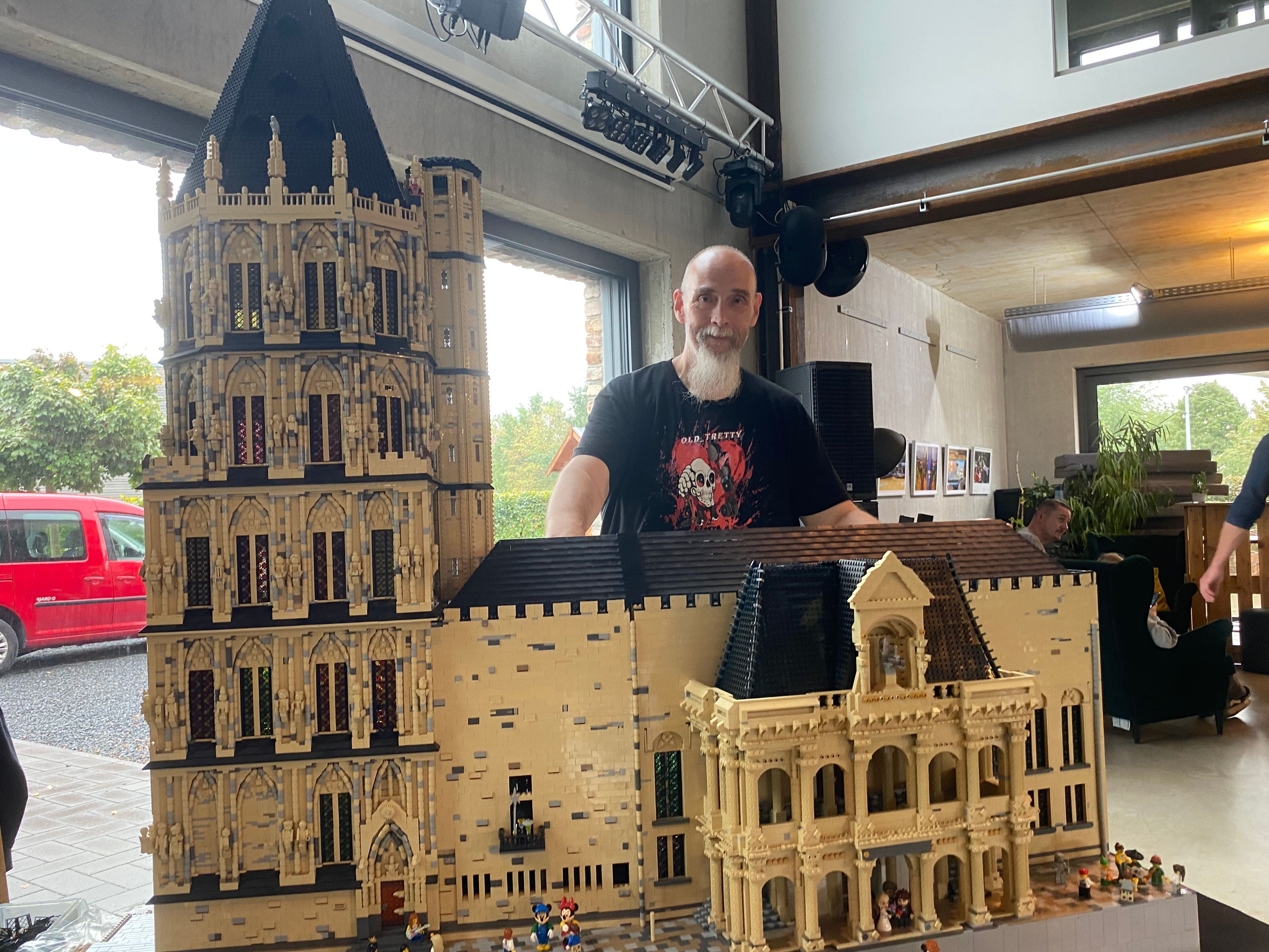 Ein Mann steht hinter dem historischen Kölner Rathaus aus Lego-Steinen.
