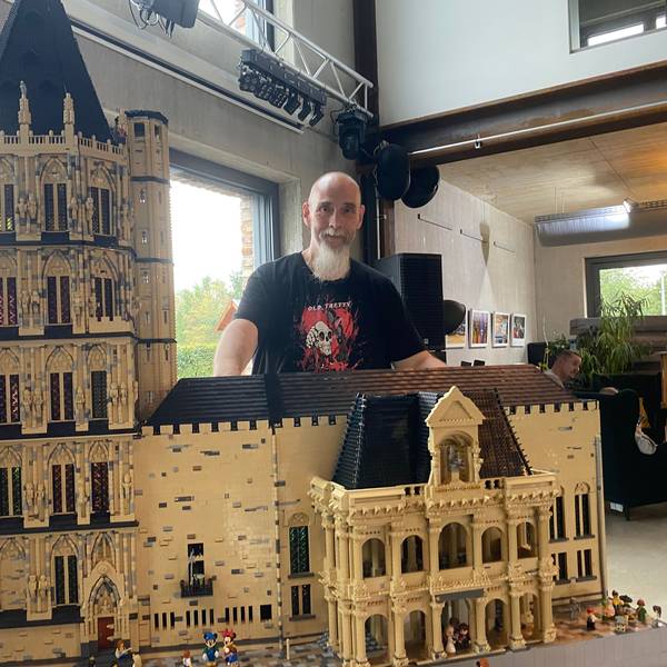 Ein Mann steht hinter dem historischen Kölner Rathaus aus Lego-Steinen.