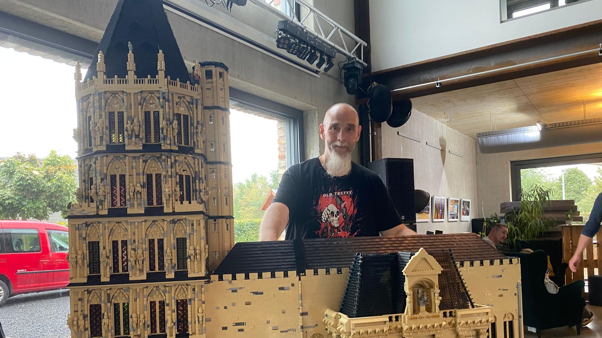 Ein Mann steht hinter dem historischen Kölner Rathaus aus Lego-Steinen.