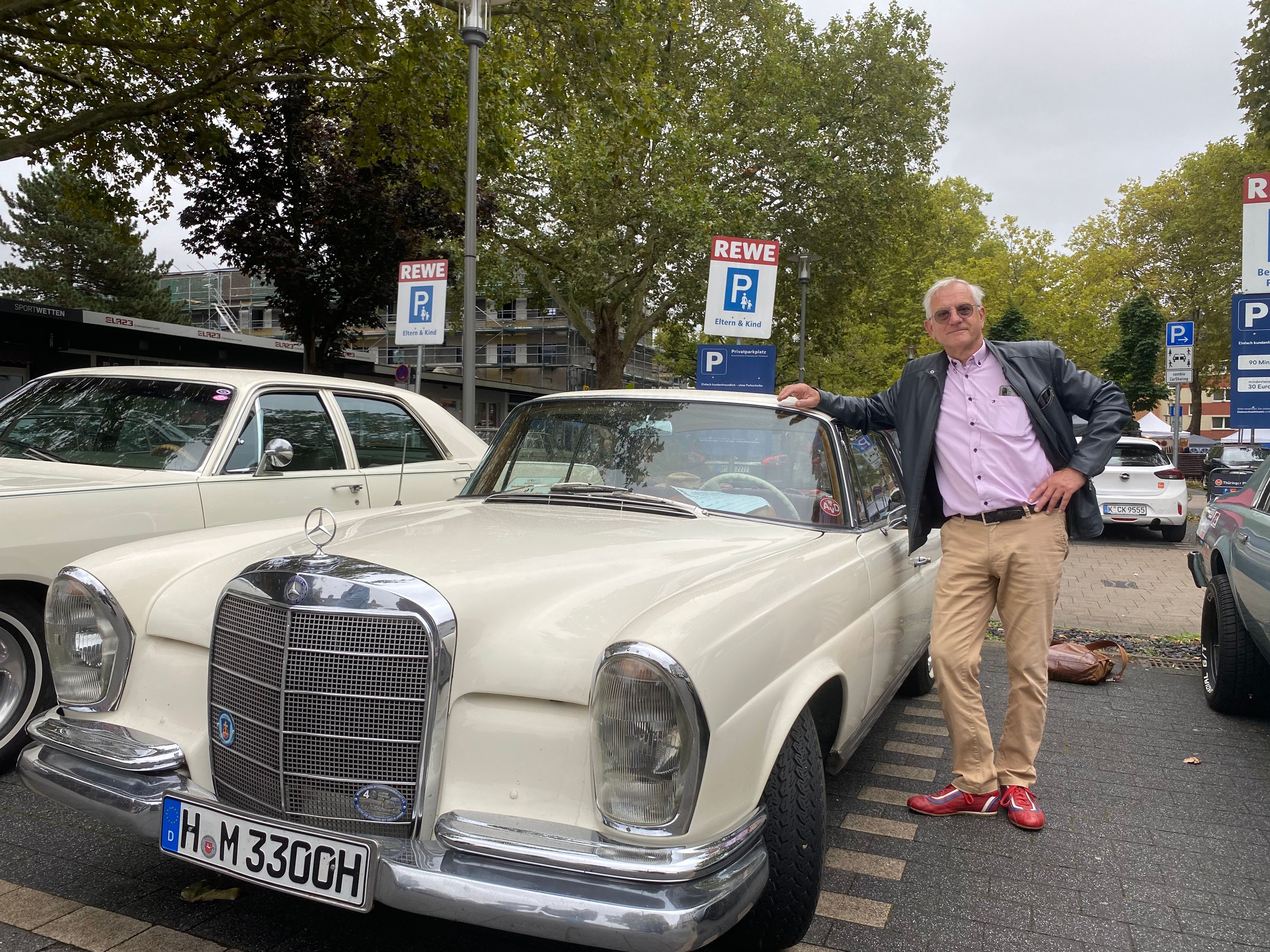 Ein Mann lehnt sich an ein cremefarbenes Mercedes-Coupé.