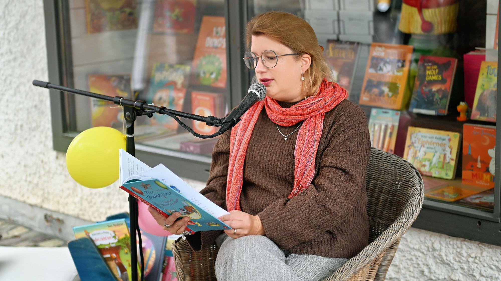 Kathrin Henk sitzt lesend in einem Sessel vor dem Schaufenster der Buchhandlung.