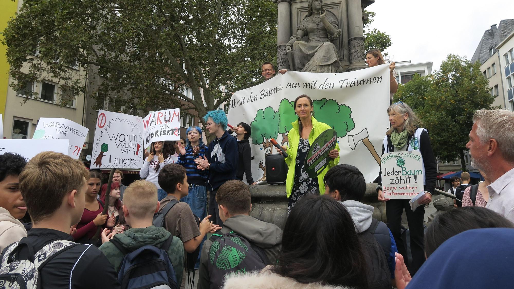 Junge Leute und vereinzelte Erwachsene stehen mit Transparenten um ein Denkmal herum.