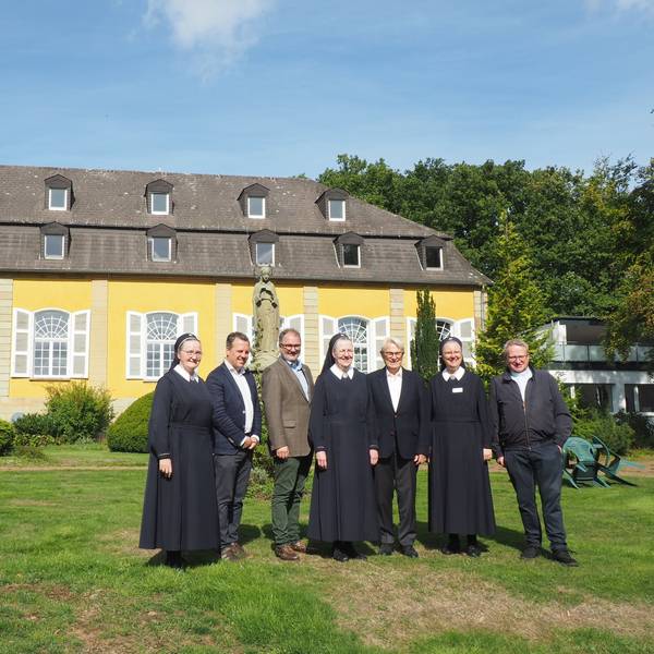 Eine Gruppe Menschen steht auf einer Wiese vor dem Haupthaus vonm Maria Wald.