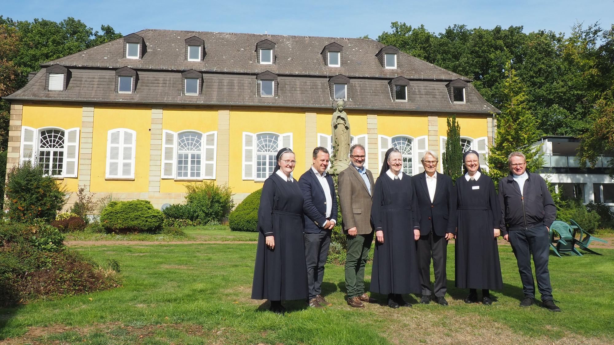 Eine Gruppe Menschen steht auf einer Wiese vor dem Haupthaus vonm Maria Wald.