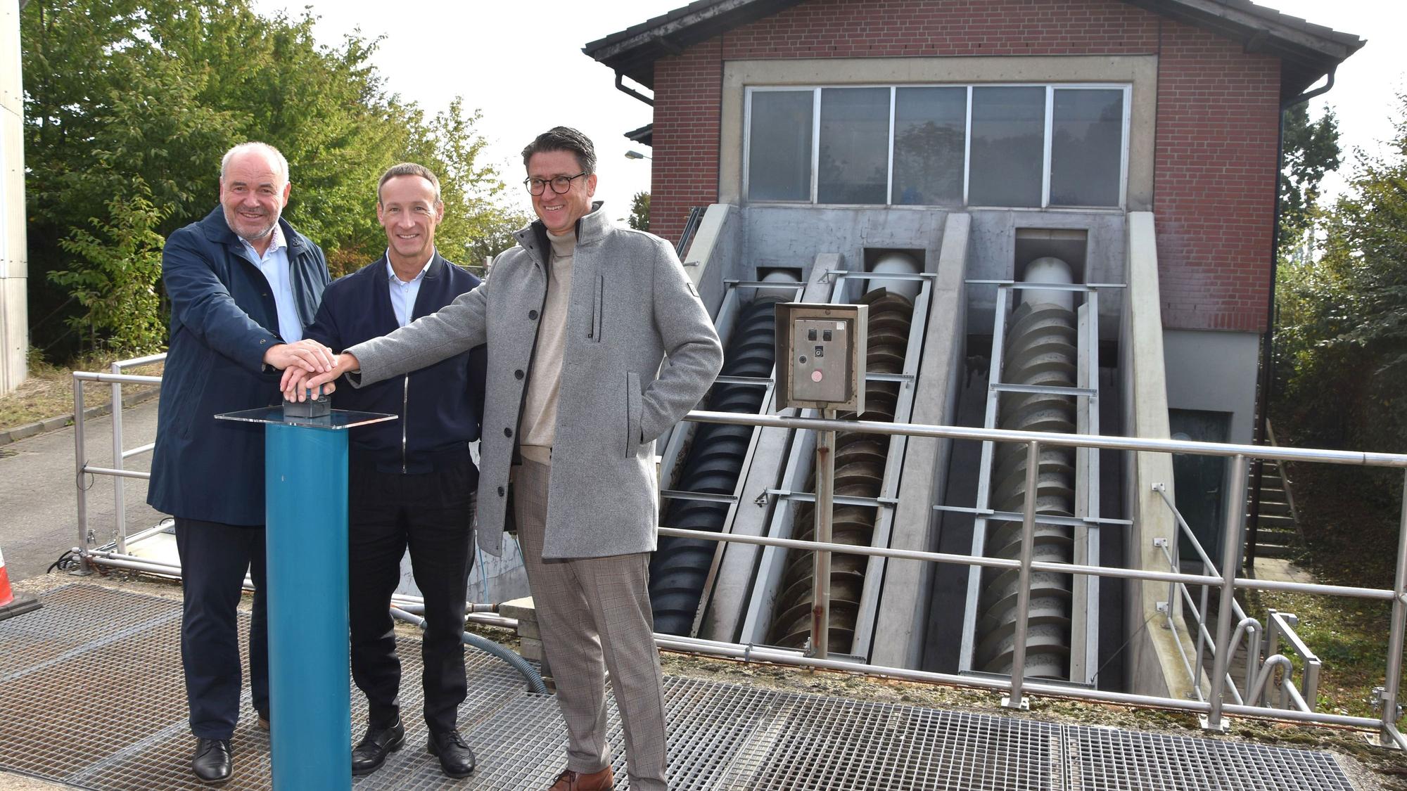 Das Foto zeigt drei Männer vor einem Klärwerk, die einen Buzzer drücken.