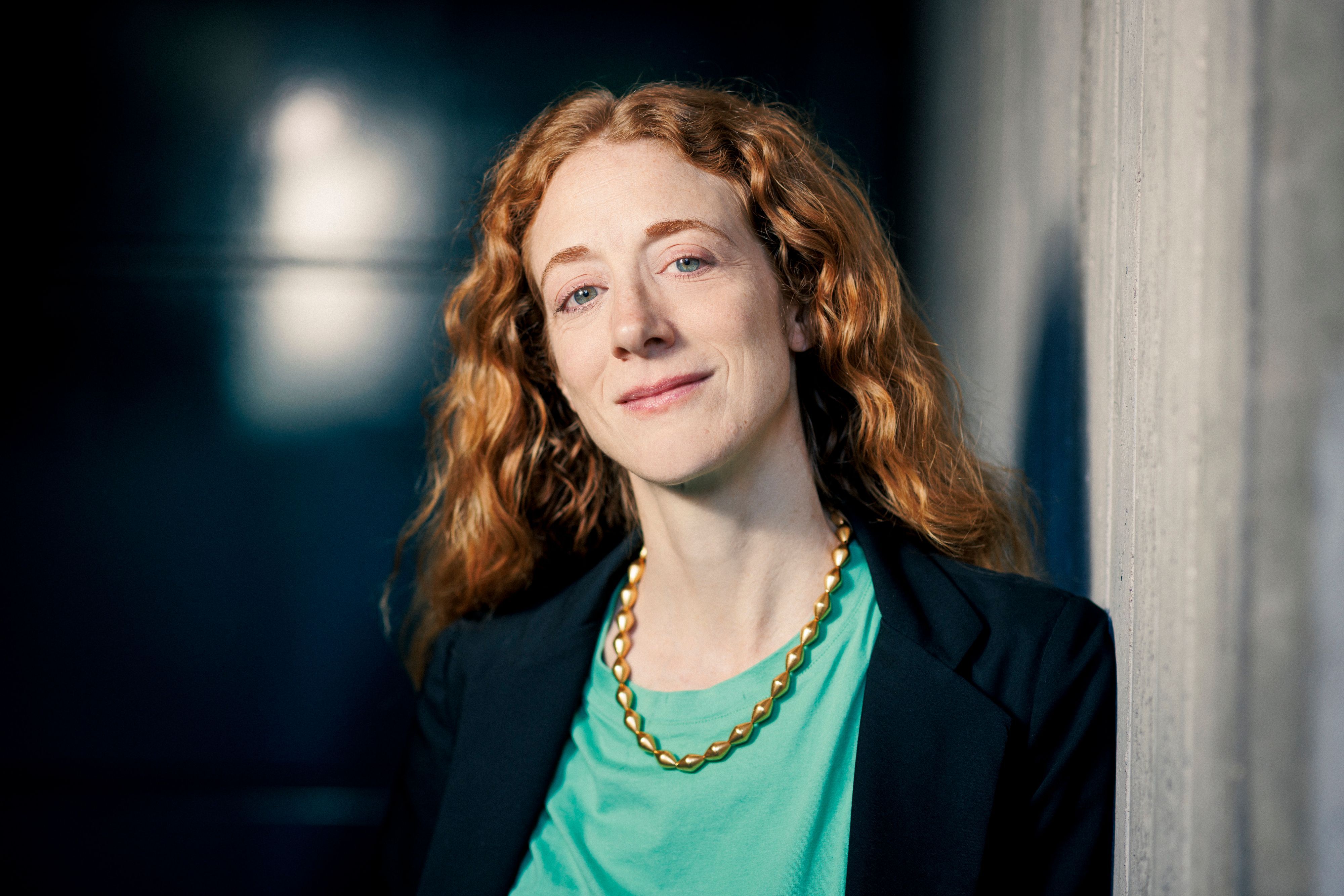Lily Sykes im Porträt. Sie lächelt, trägt einen dunklen Blazer und eine grüne Bluse, die mit ihren roten Haaren kontrastiert.