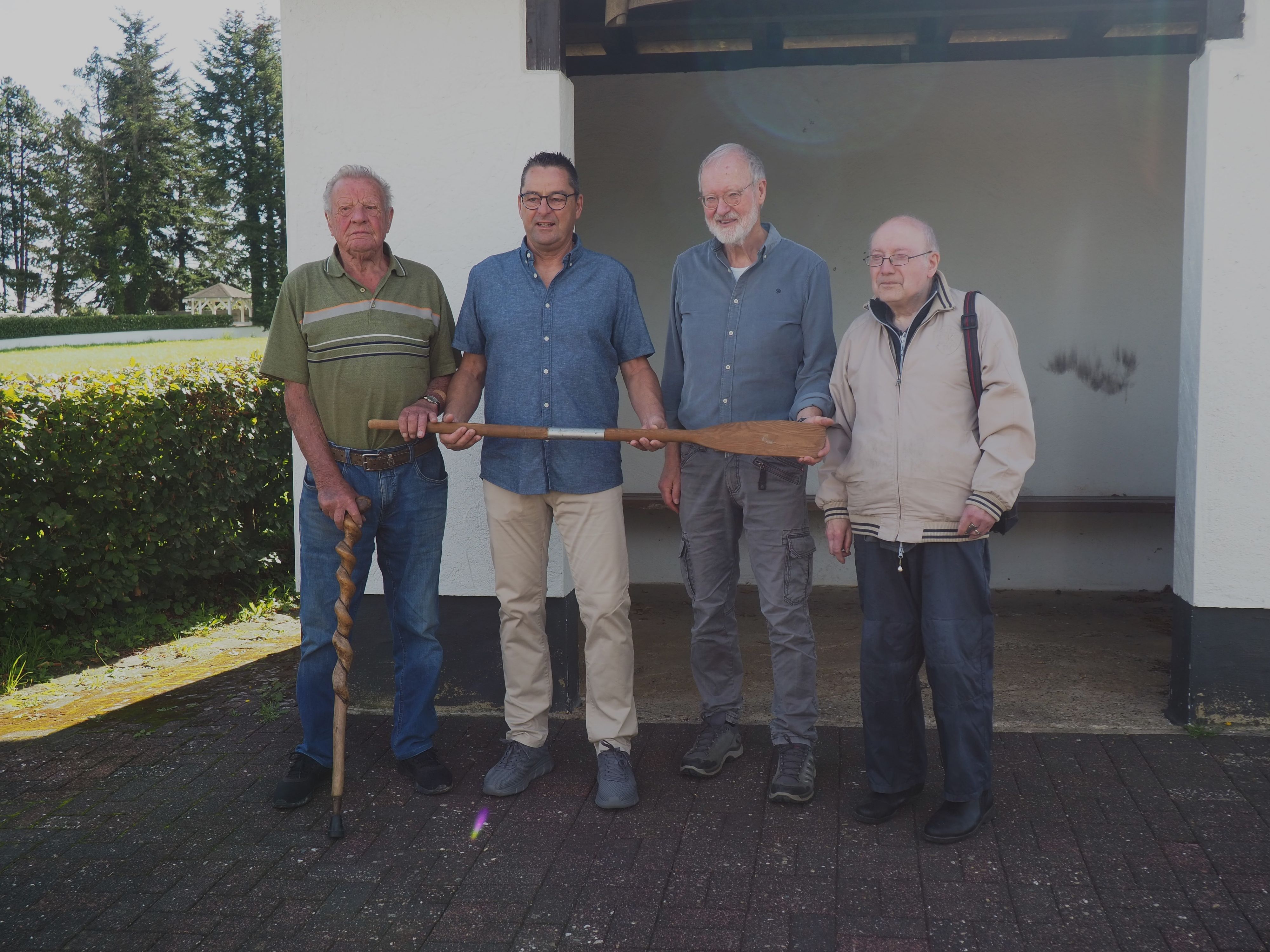 Vier Männer stehen nebeneinander, zwei halten ein Paddel.