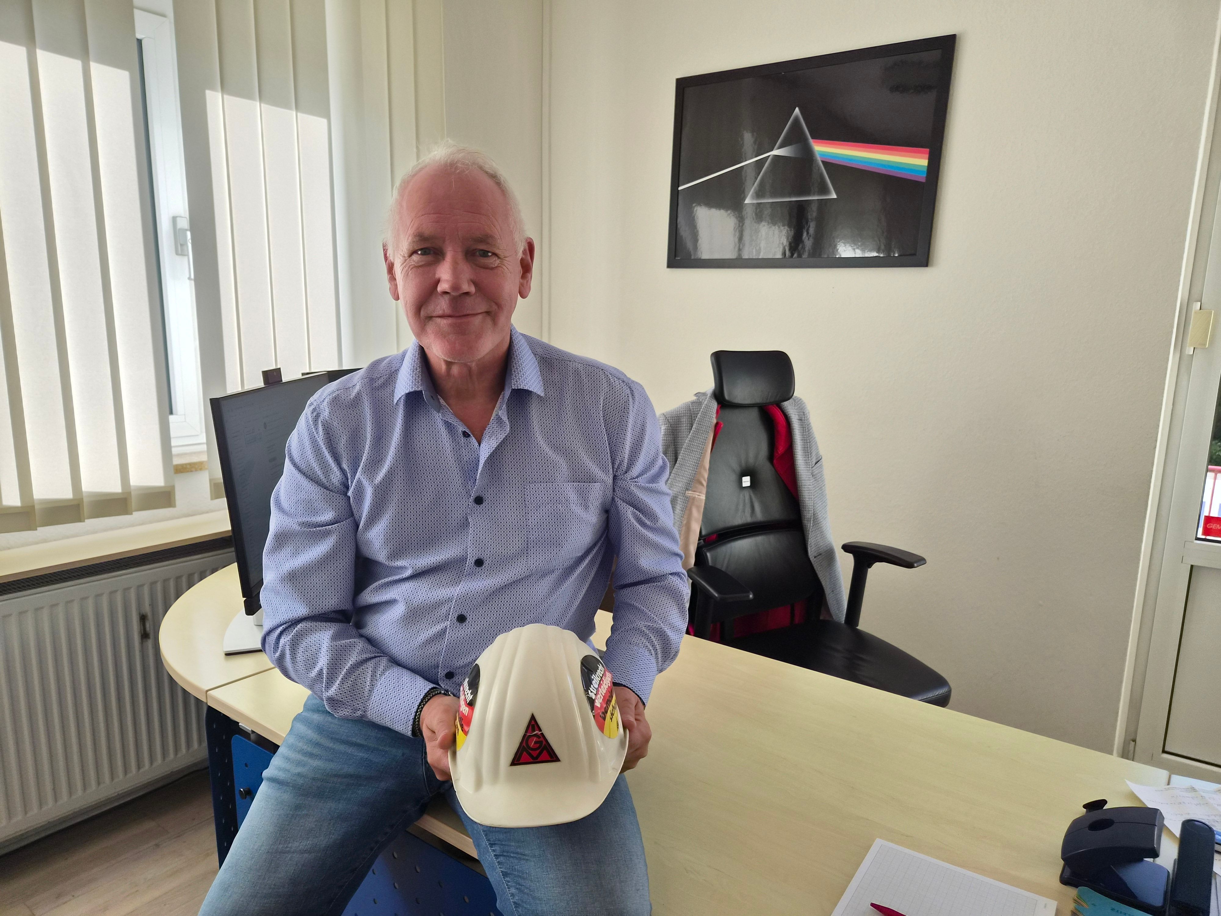 Ein Mann sitzt am Schreibtisch und hält einen Helm in der Hand.