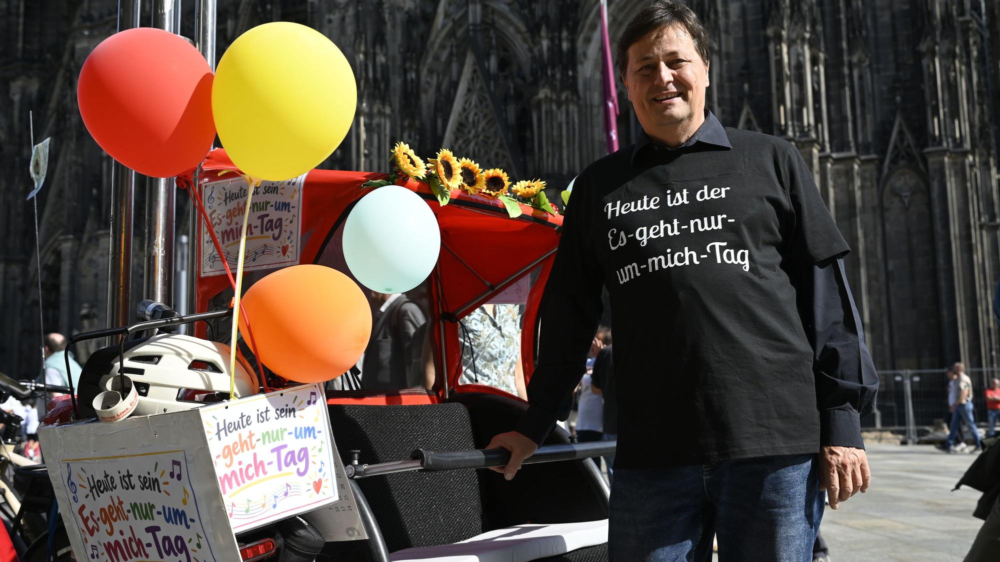Ein Mann mit schwarzem Shirt und schwarzen Haaren steht neben einer geschmückten Rikscha vor dem Dom.