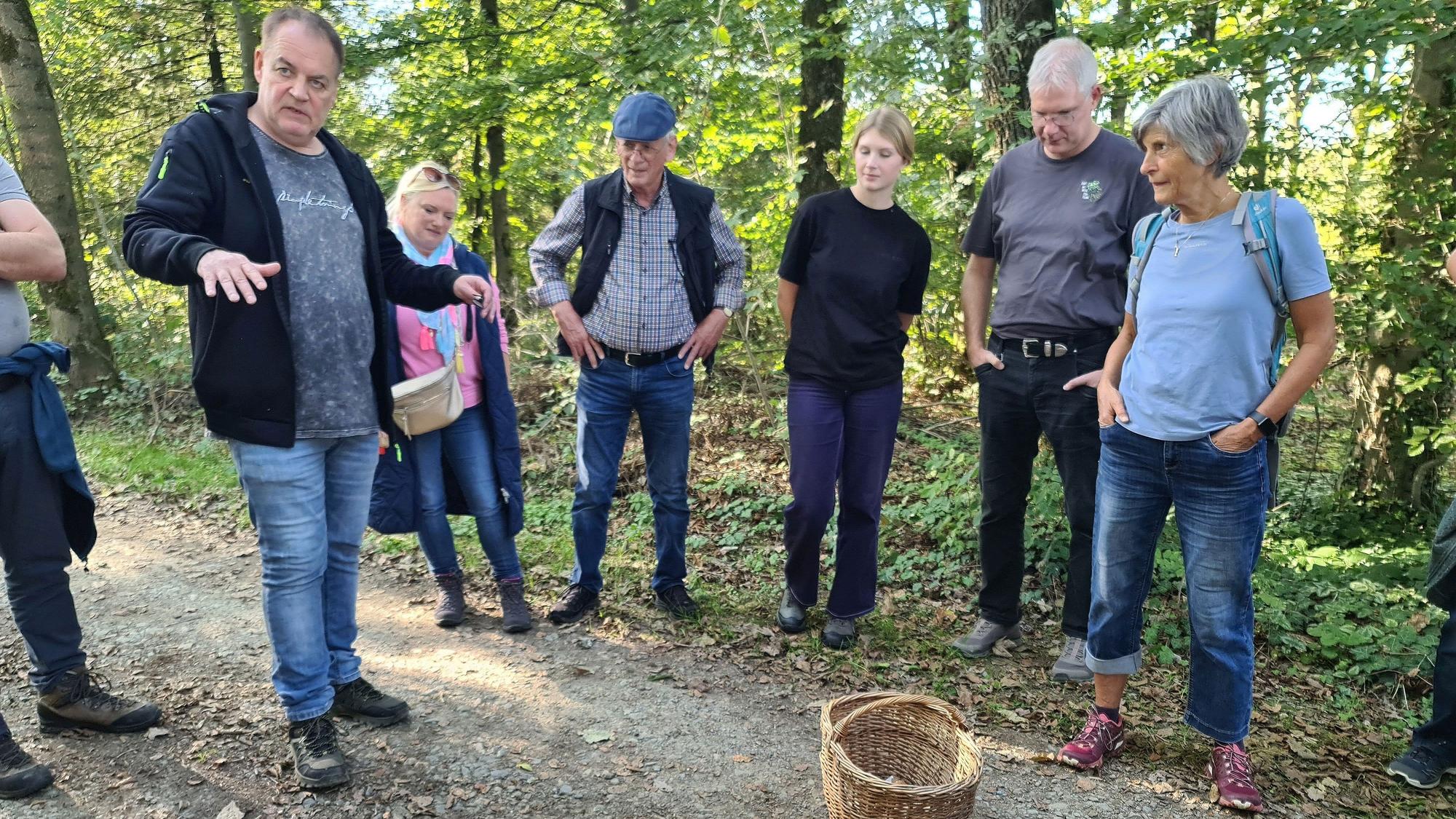 Ein Mann spricht im Wald vor einer Gruppe und einem Bastkorb stehend.