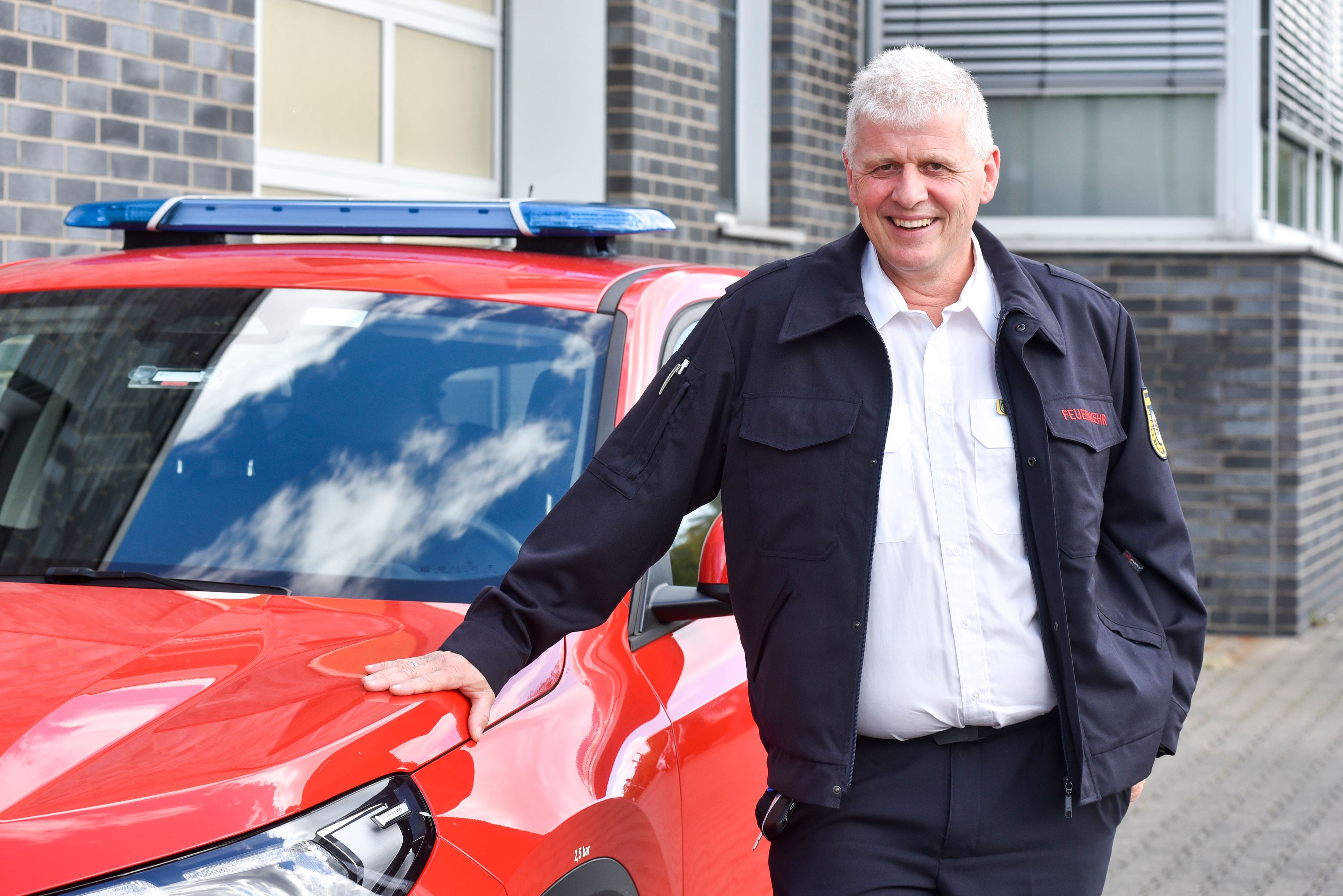 Ein Mann steht neben einem roten Auto.