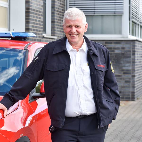 Ein Mann steht neben einem roten Auto.