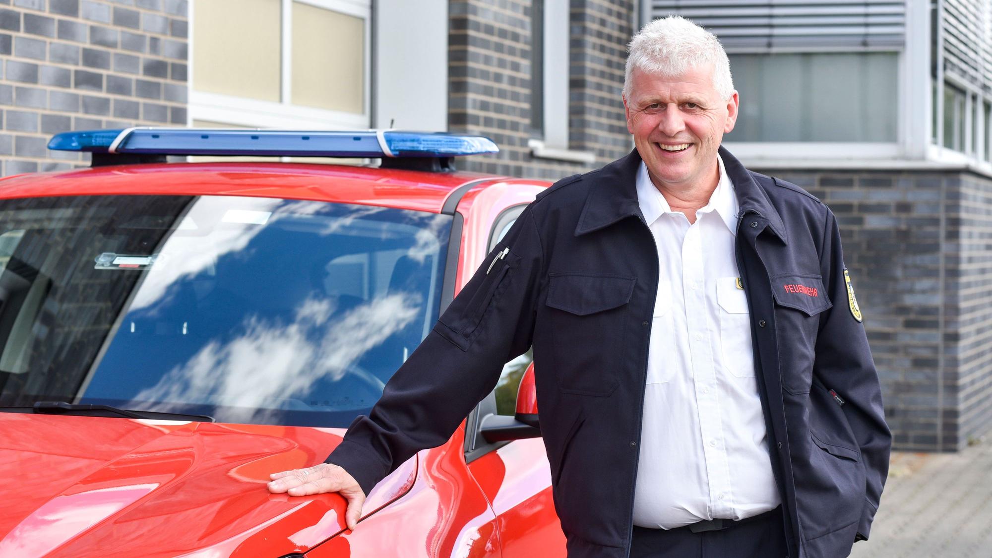 Ein Mann steht neben einem roten Auto.