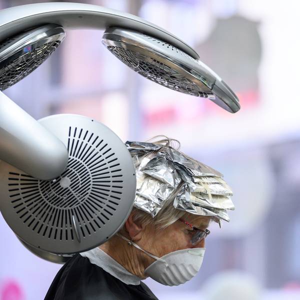 Eine Kundin mit Mund- und Nasenschutz sitzt in einem Friseursalon unter einem Trockengerät.