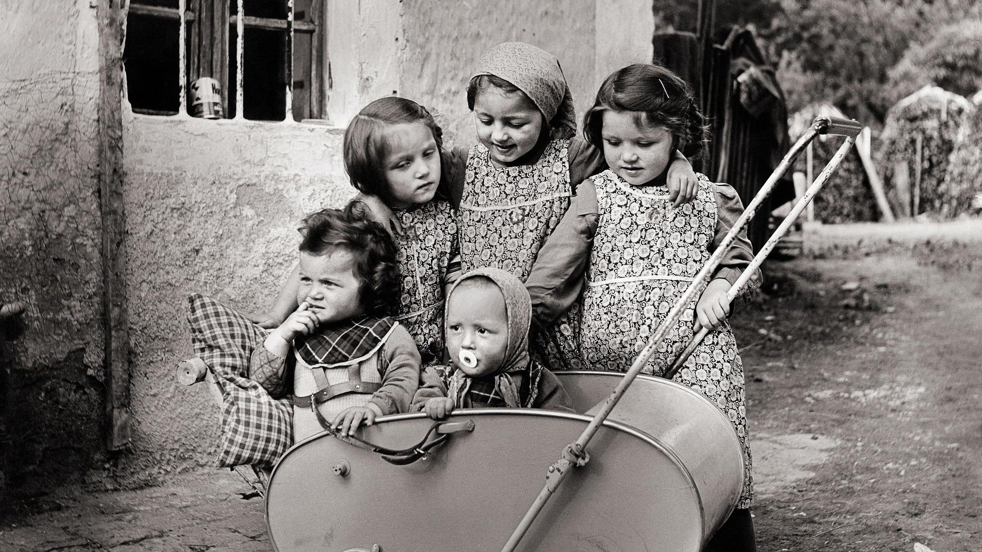 Fünf Mädchen stehen um einen Kinderwagen herum.