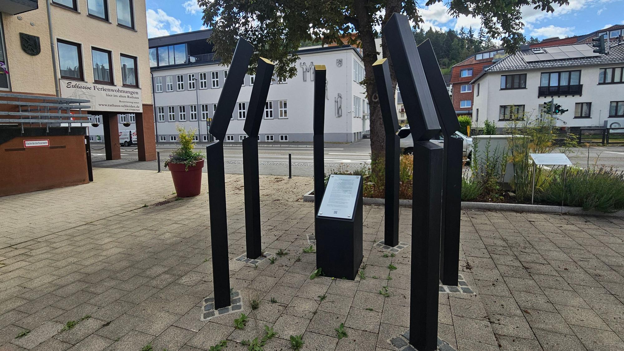 Das Foto zeigt sechs Eisenstelen mit einer Tafel in der Mitte.