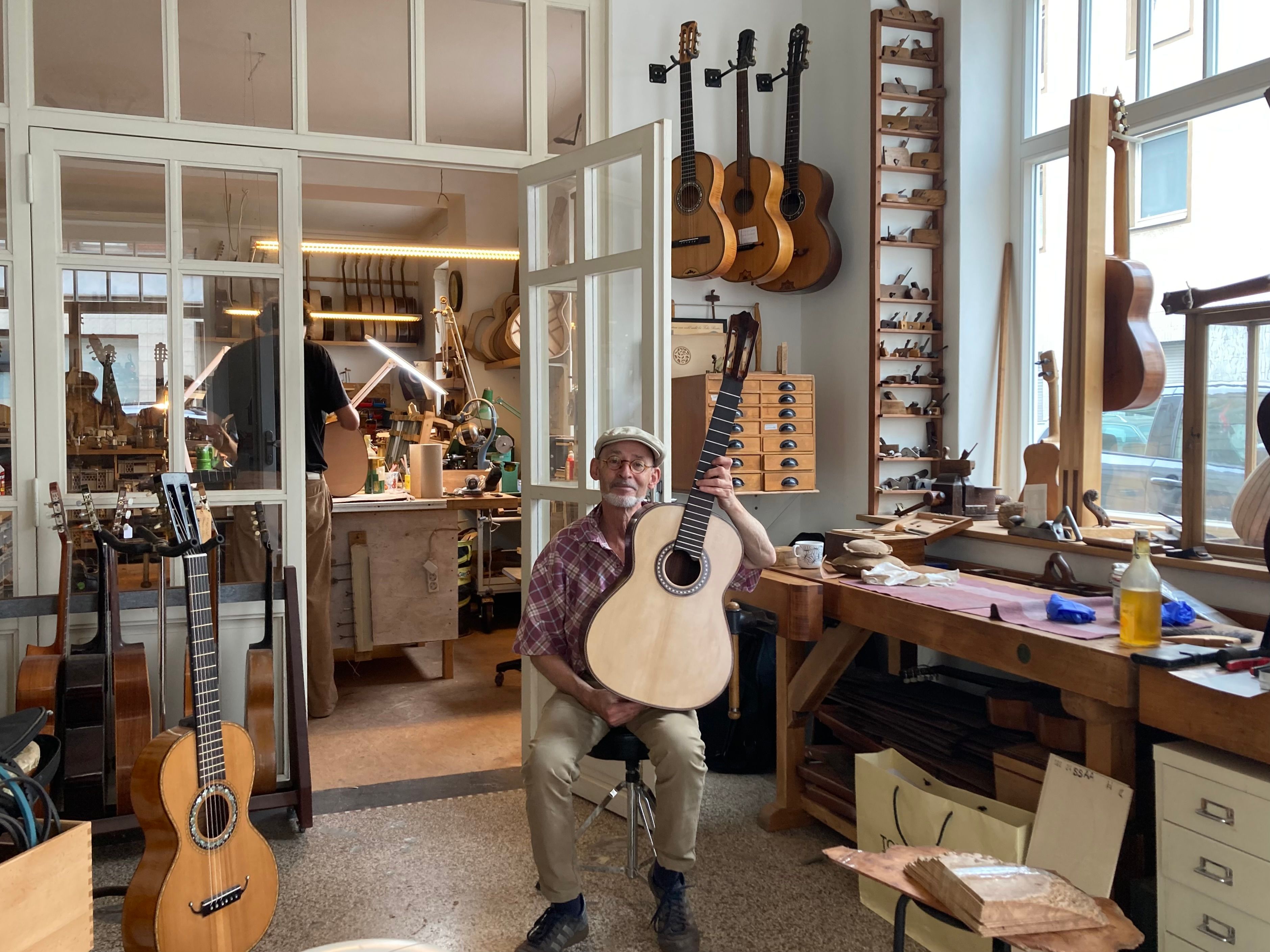 Ein Gitarrenbauer sitzt in seinem Atelier und hält eine Gitarre.