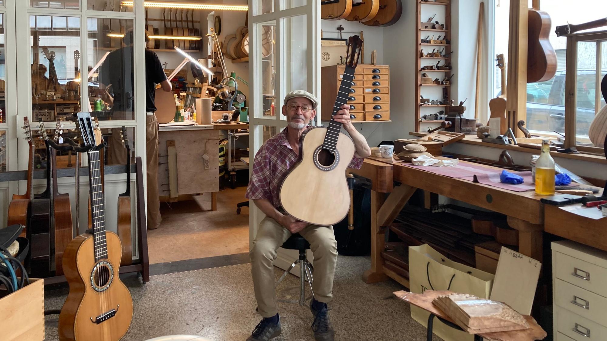 Ein Gitarrenbauer sitzt in seinem Atelier und hält eine Gitarre.