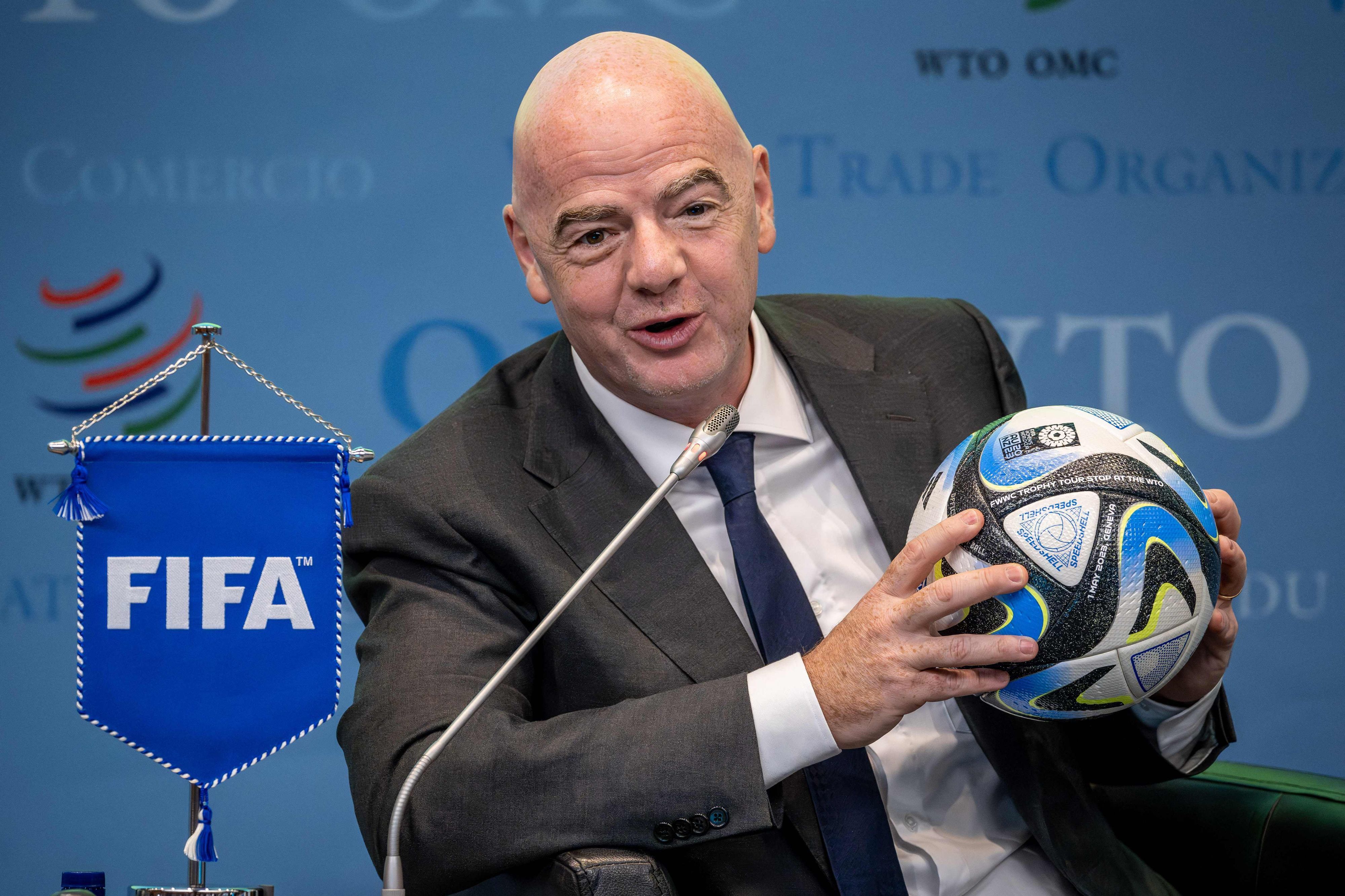 Bei einer Pressekonferenz hält Gianni Infantino einen Ball in der Hand.