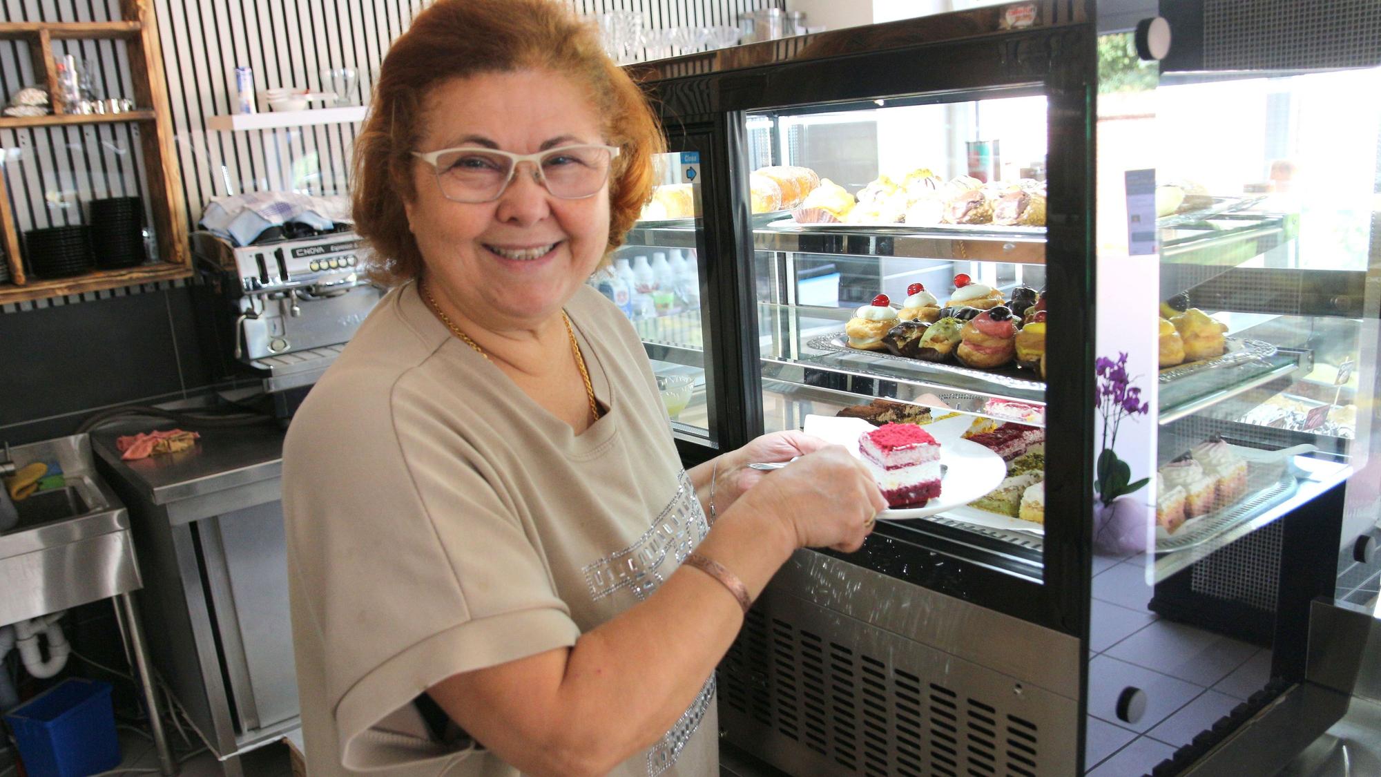 Eine Frau lächelt in die Kamera, in der Hand hält sie einen Teller mit einem Stück Kuchen.