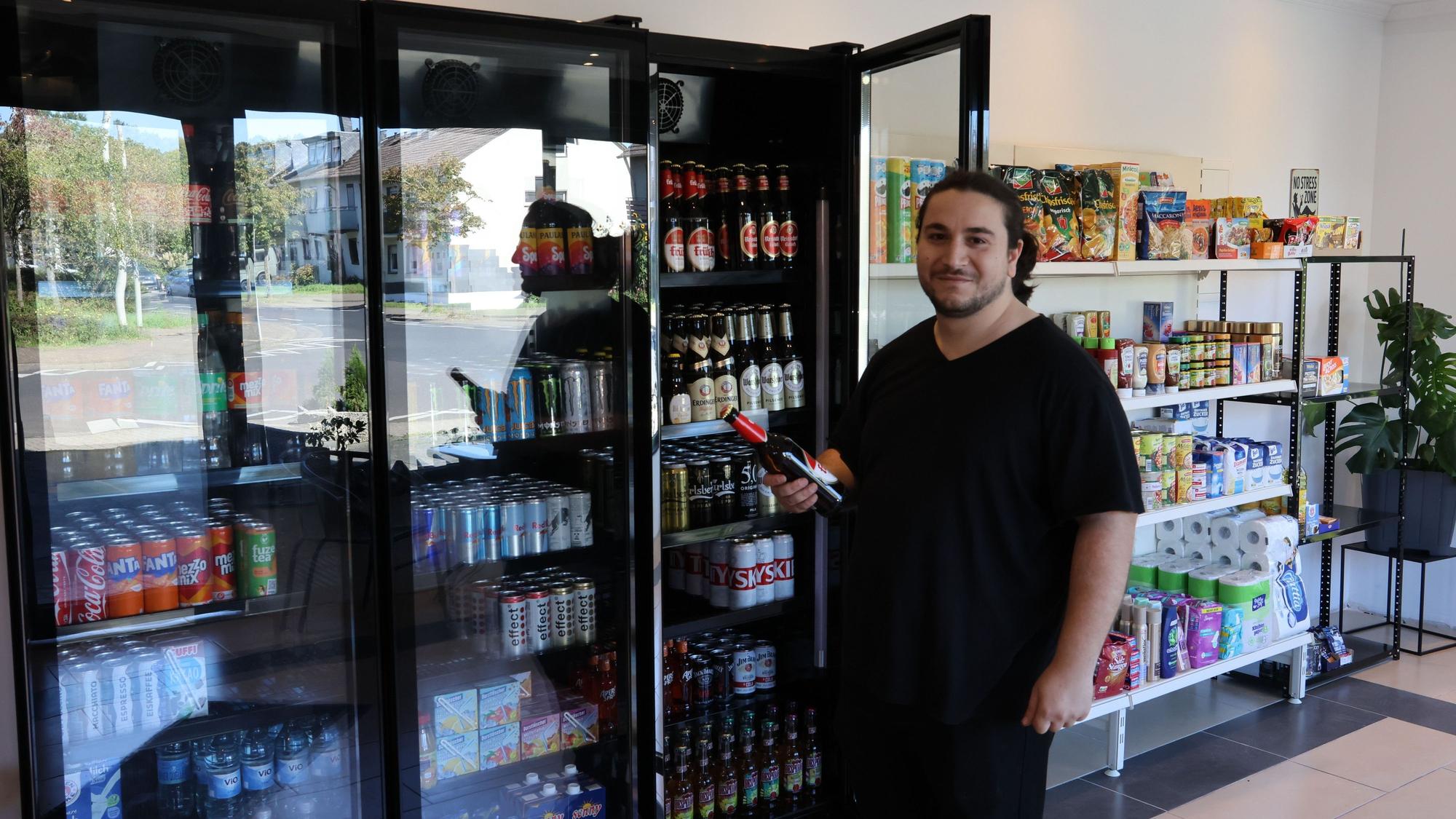 Zu sehen ist Safak Mutlu, erhält vor einem geöffneten Kühlschrank eine Flasche in der Hand.
