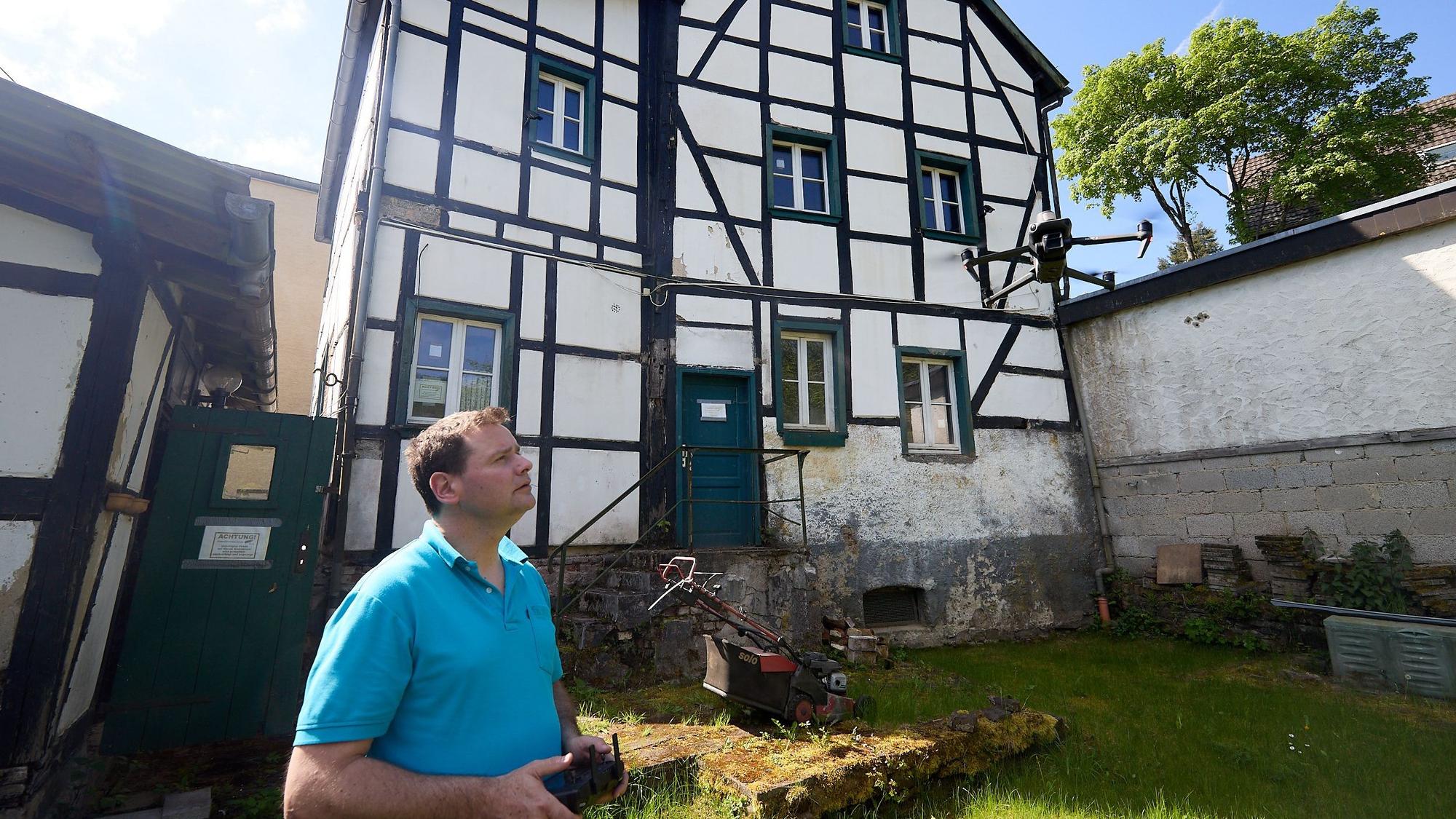 Hans Meyer steuert eine Drohne, im Hintergrund ist ein altes Fachwerkhaus zu sehen.