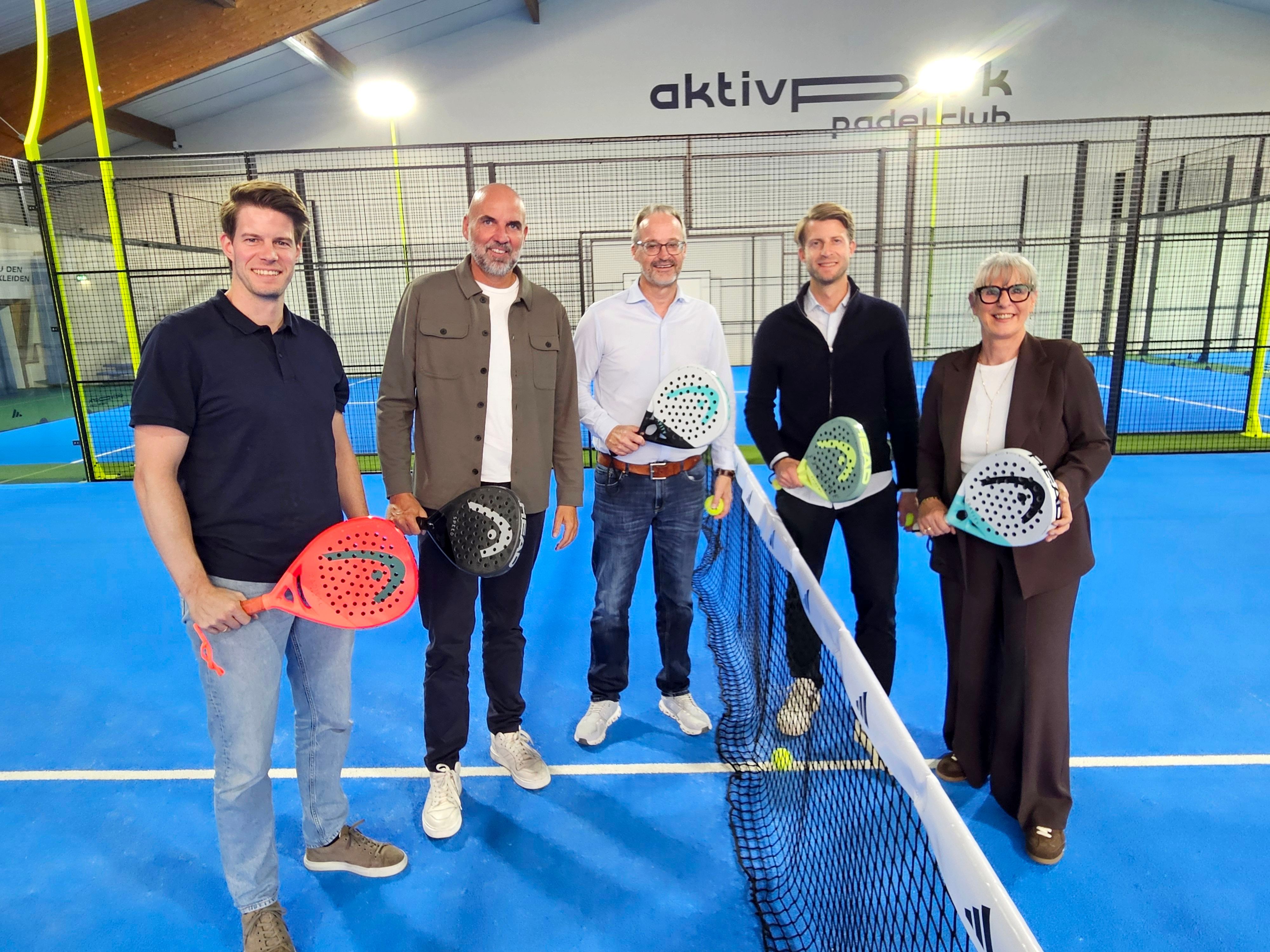 Vier Männer und eine Frau mit Padel-Schlägern stehen am Netz.