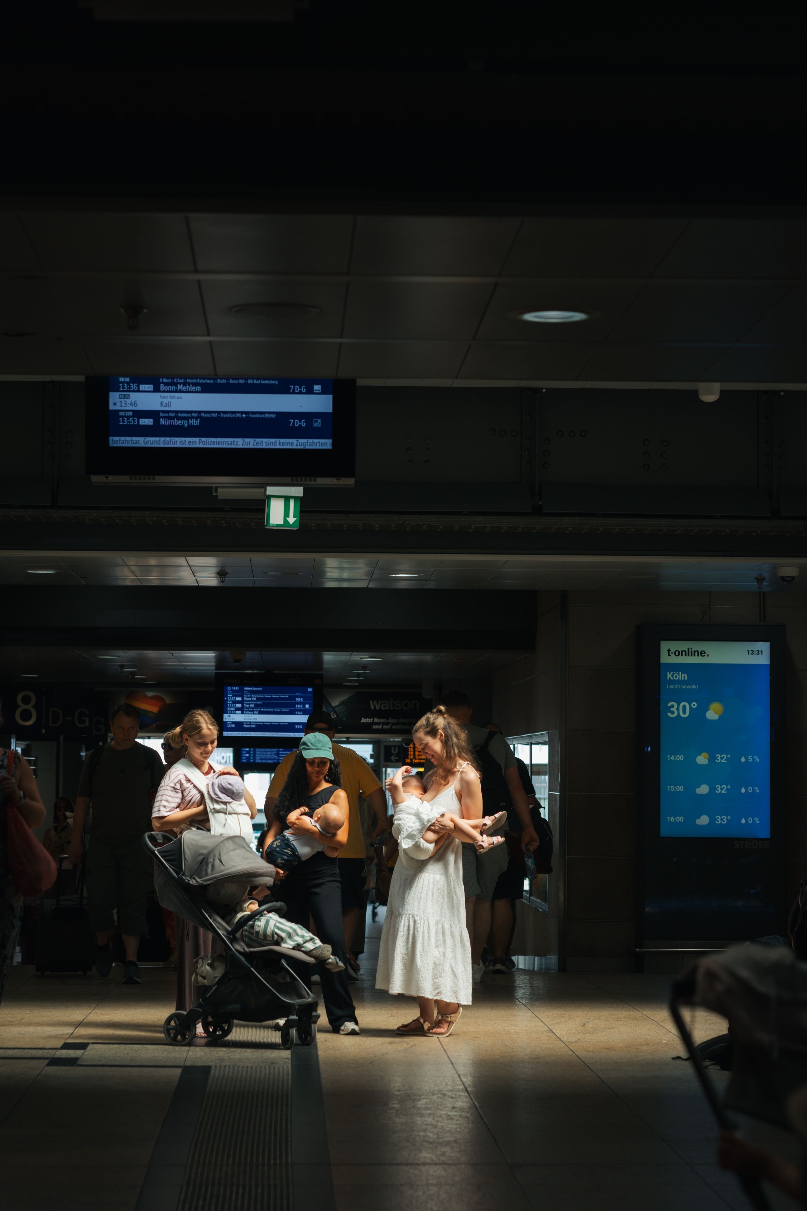 Drei Frauen stehen im Kölner Hauptbahnhof und stillen ihre Kinder.