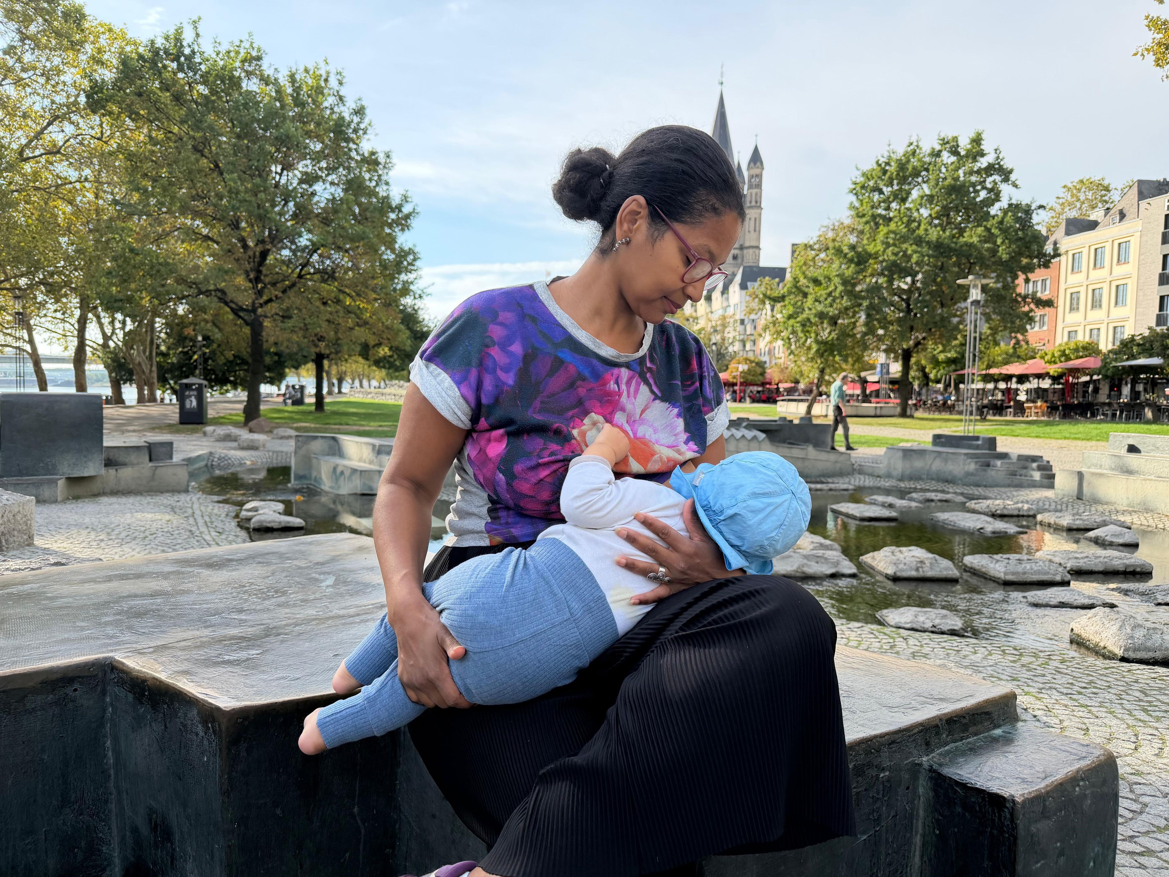 Eugenia Diarra sitzt im Rheingarten in der Altstadt in Köln und stillt ihr Baby.