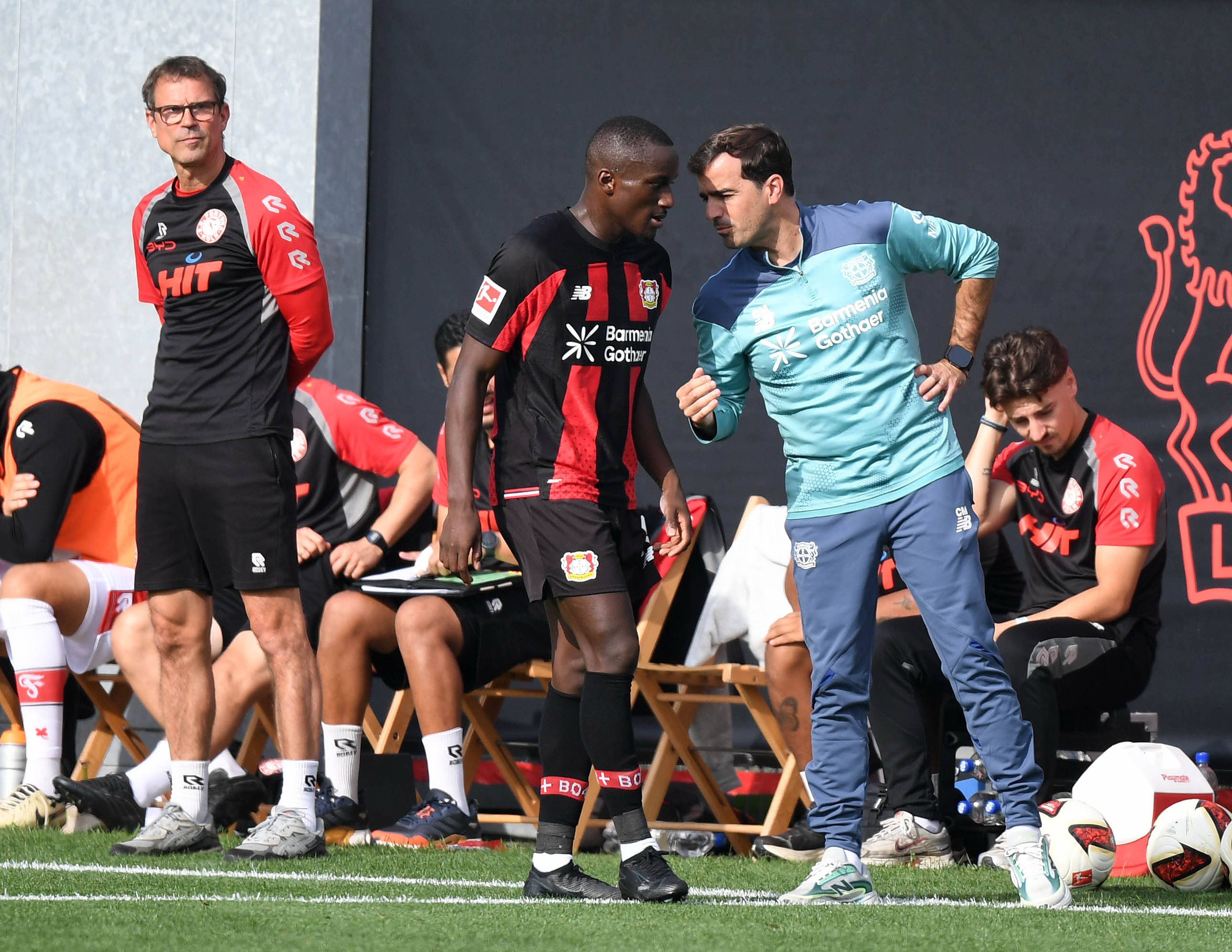 Carles Martínez (r.) gibt Moussa Diaby Anweisungen. Fortuna Kölns Trainer Matthias Mink beobachtet das Spielgeschehen (l.).
