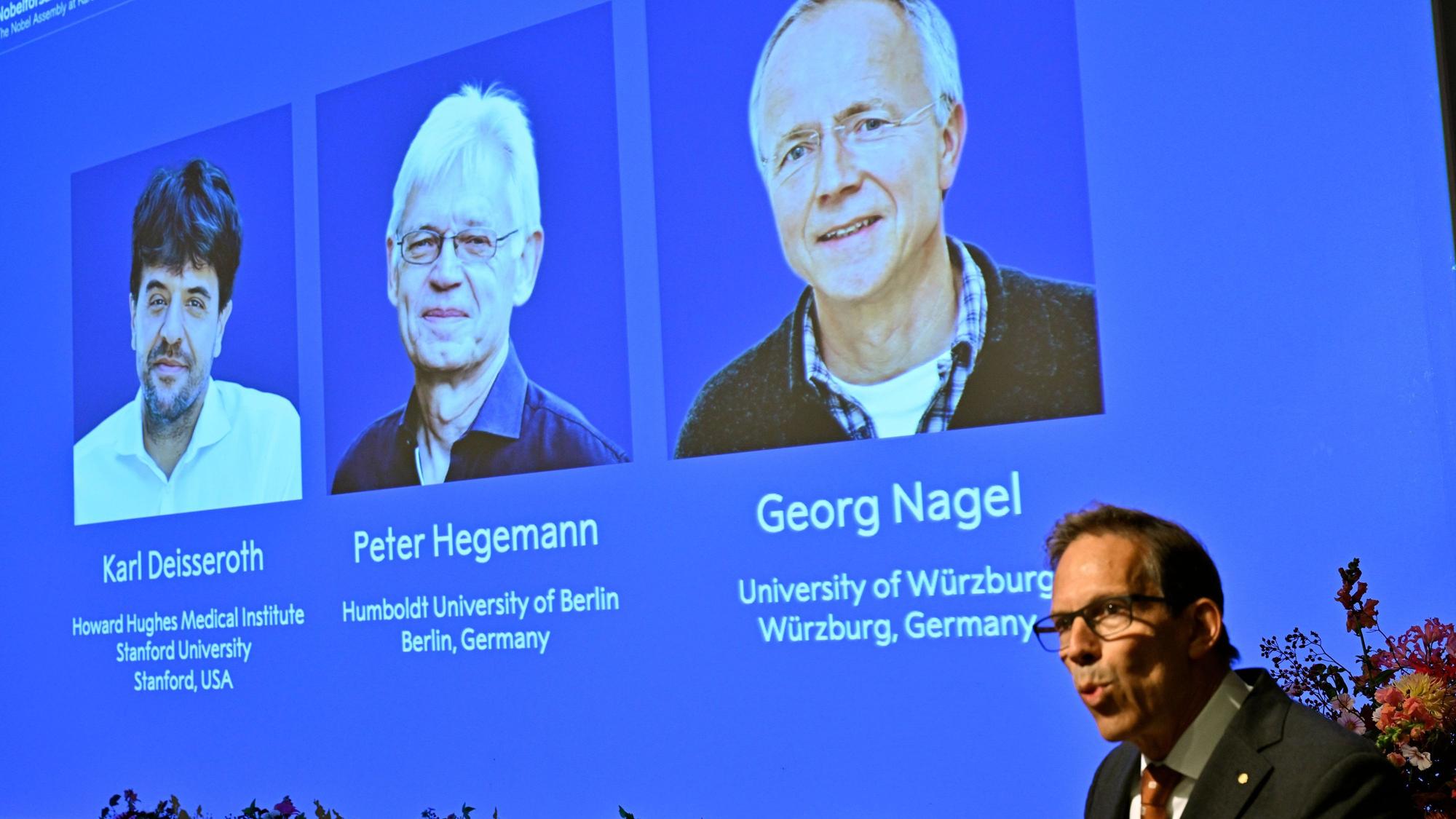 Karl Deisseroth, Peter Hegemann und Georg Nagel sind auf dem Bildschirm zu sehen, als ihnen der Nobelpreis für Physiologie oder Medizin 2026 verliehen wird.