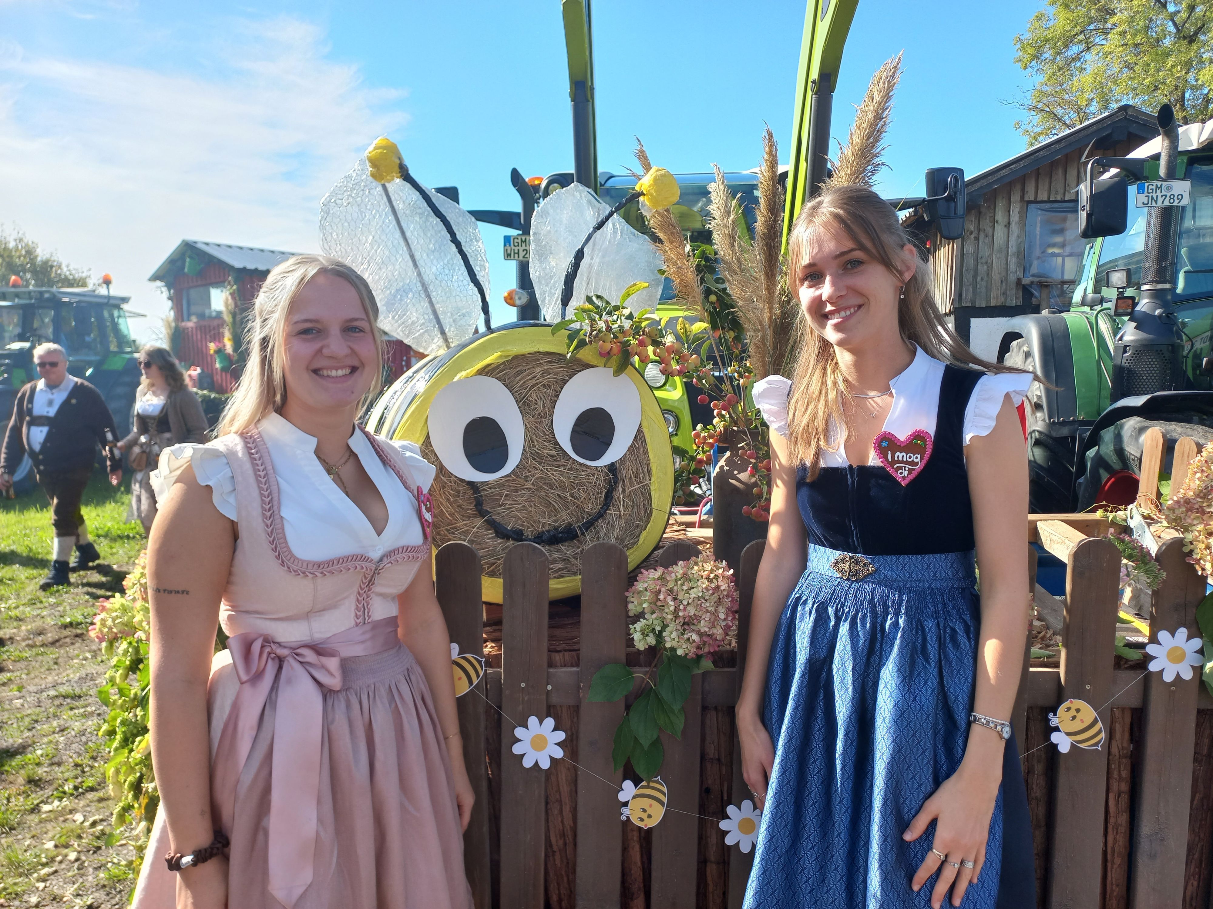 Zwei junge Frauen stehen vor einem Erntewagen.