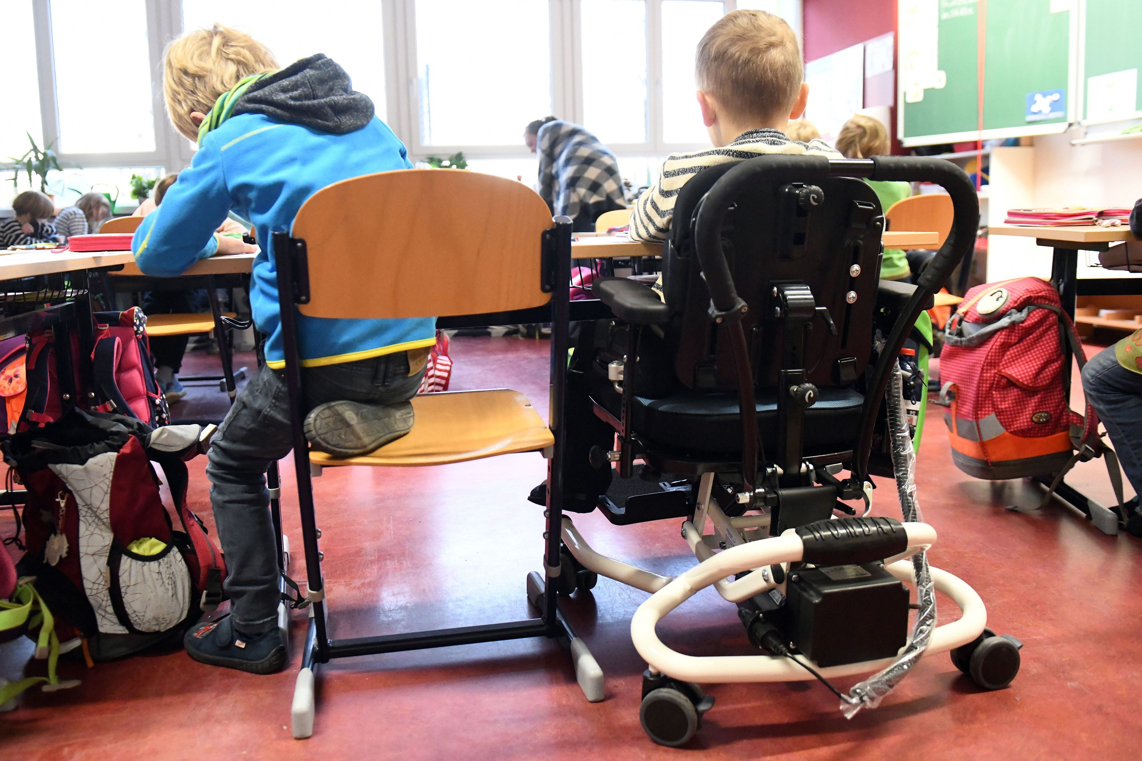 Ein Kind mit Behinderung sitzt in seinem Rollstuhl gemeinsam mit anderen Erstklässlern ohne Handicap in einem Klassenraum.