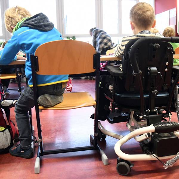 Ein Kind mit Behinderung sitzt in seinem Rollstuhl gemeinsam mit anderen Erstklässlern ohne Handicap in einem Klassenraum.