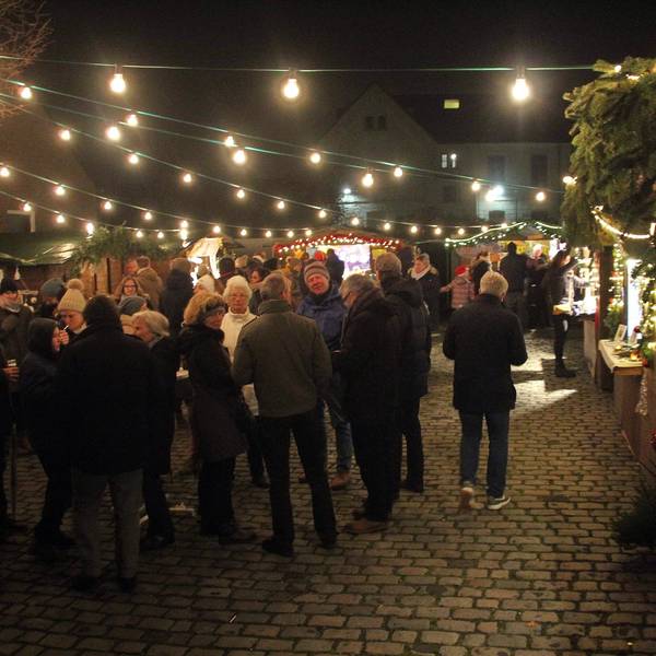 Auf einem Platz ist ein Weihnachtsmarkt mit Buden, Lichterketten und Weihnachtsbaum aufgebaut.