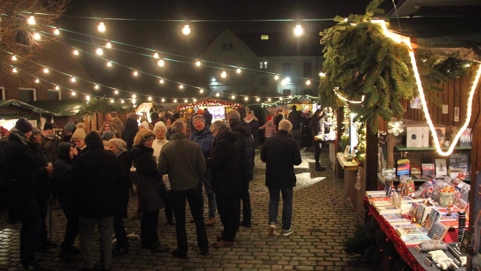 Auf einem Platz ist ein Weihnachtsmarkt mit Buden, Lichterketten und Weihnachtsbaum aufgebaut.