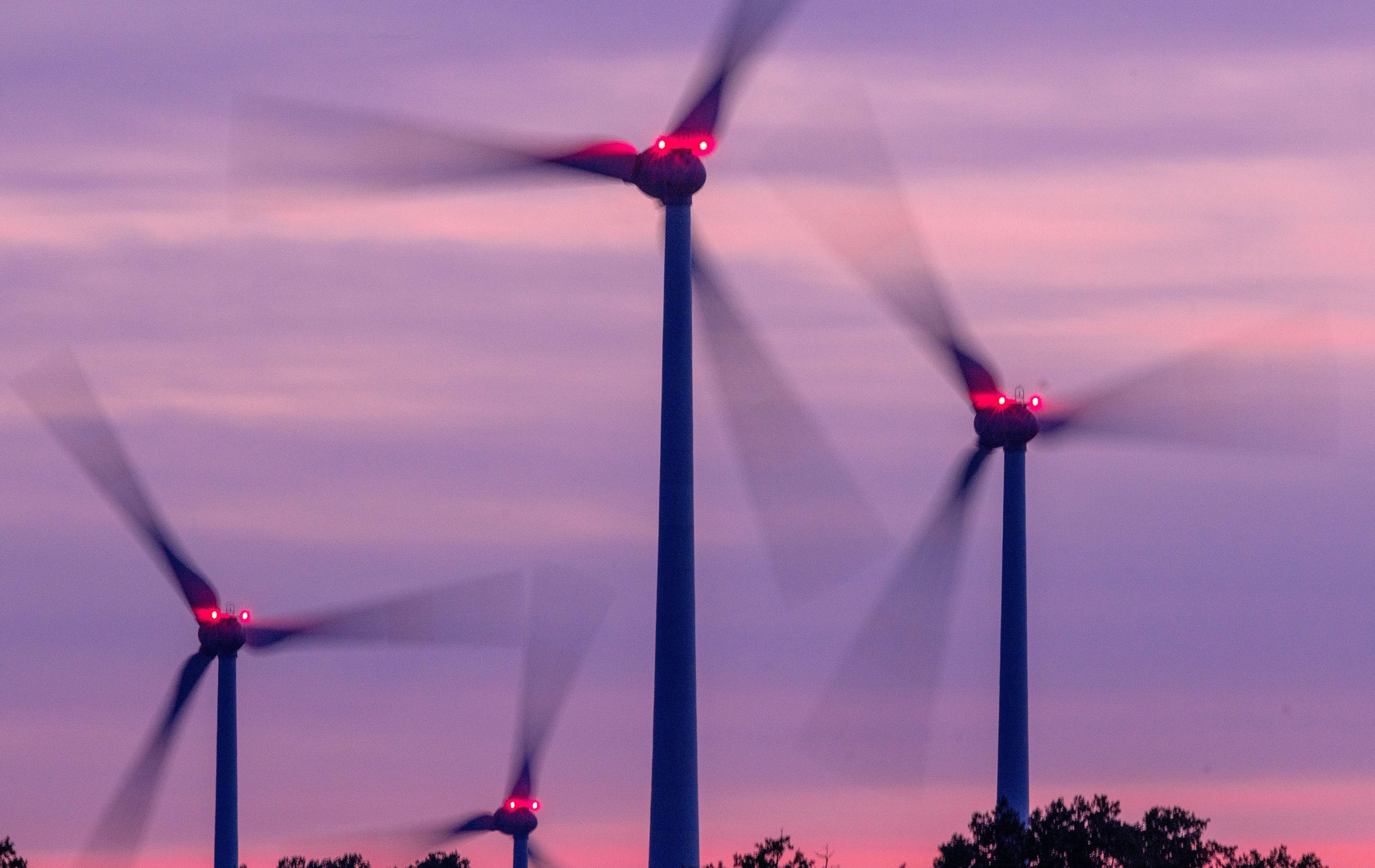 Mit Signallampen beleuchtete Windräder drehen sich nach Sonnenuntergang in einem Windpark.