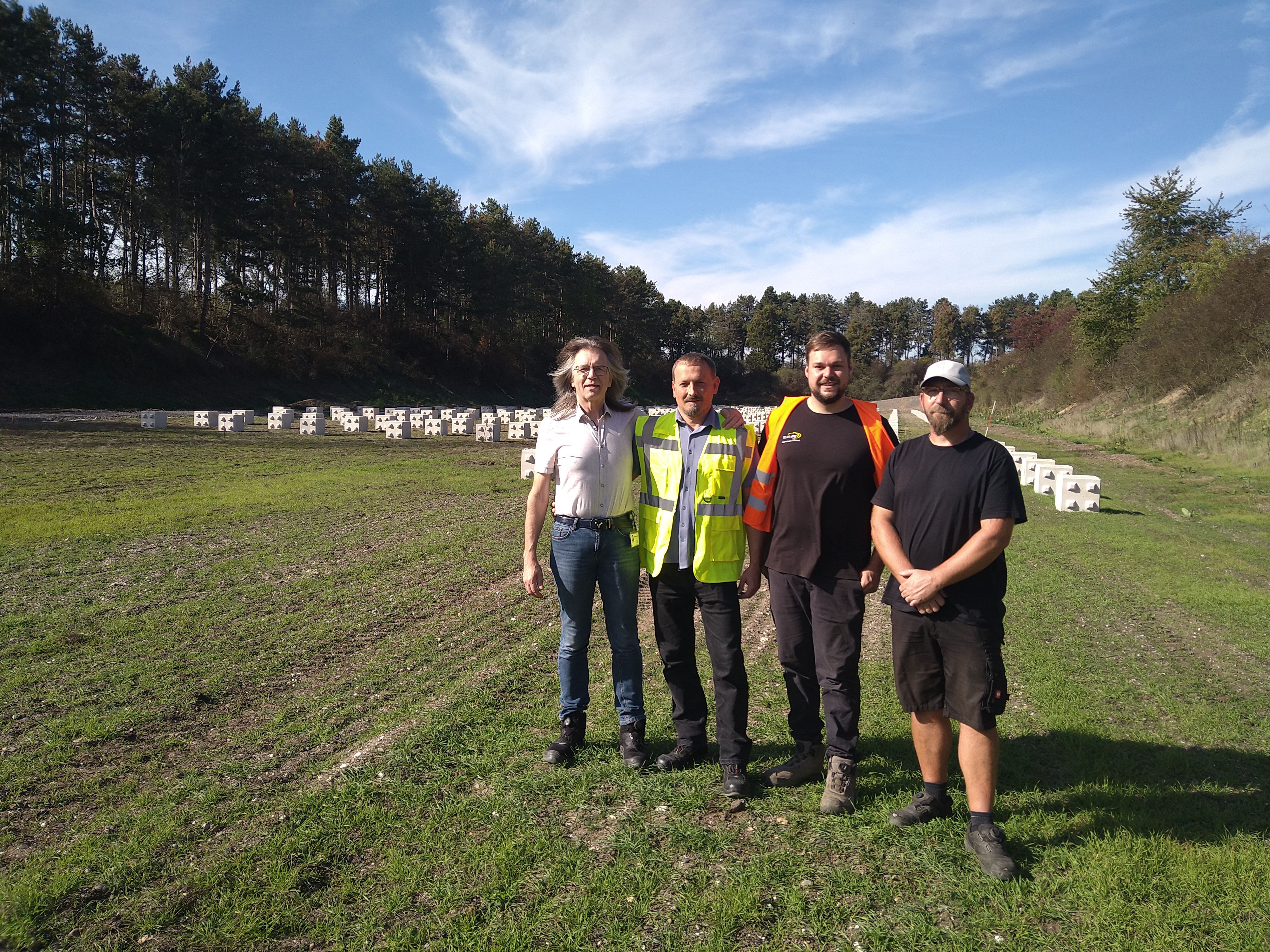 Vier Männer stehen auf einer großen Wiese, im Hintergrund sind PV-Elemente im Boden verankert.