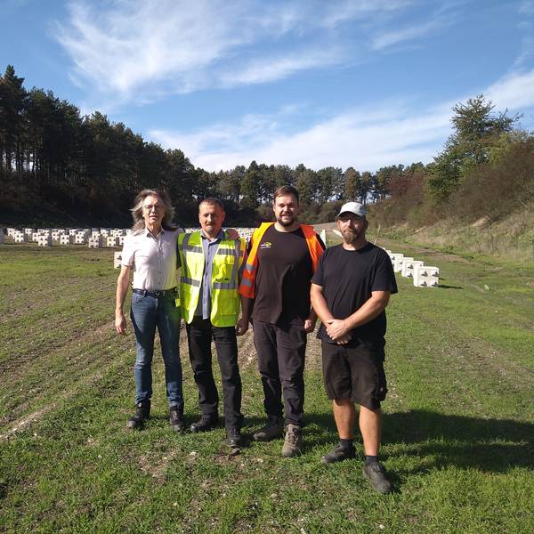 Vier Männer stehen auf einer großen Wiese, im Hintergrund sind PV-Elemente im Boden verankert.