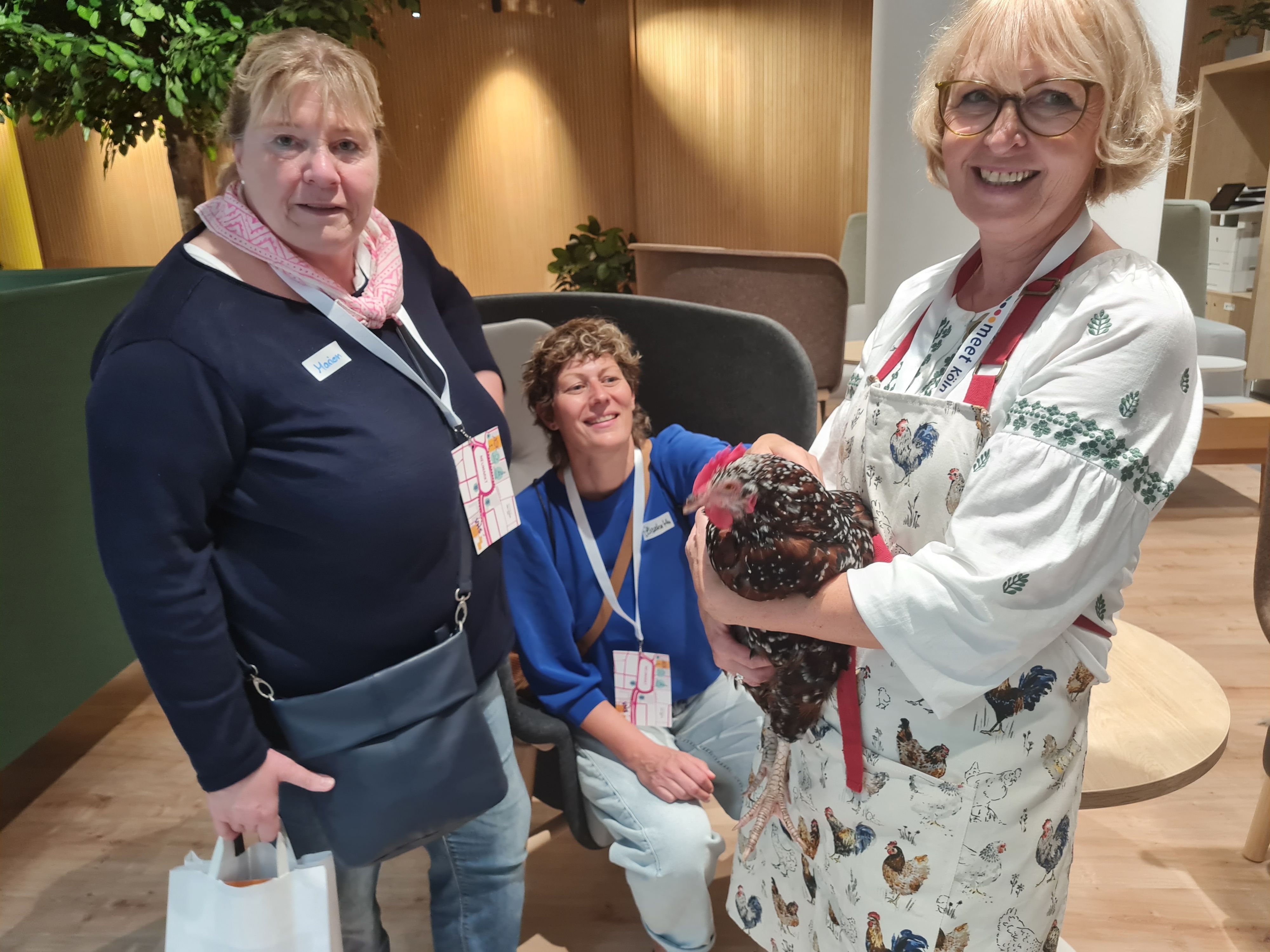Eine Frau hält ein Huhn auf dem Arm, zwei andere streicheln es.