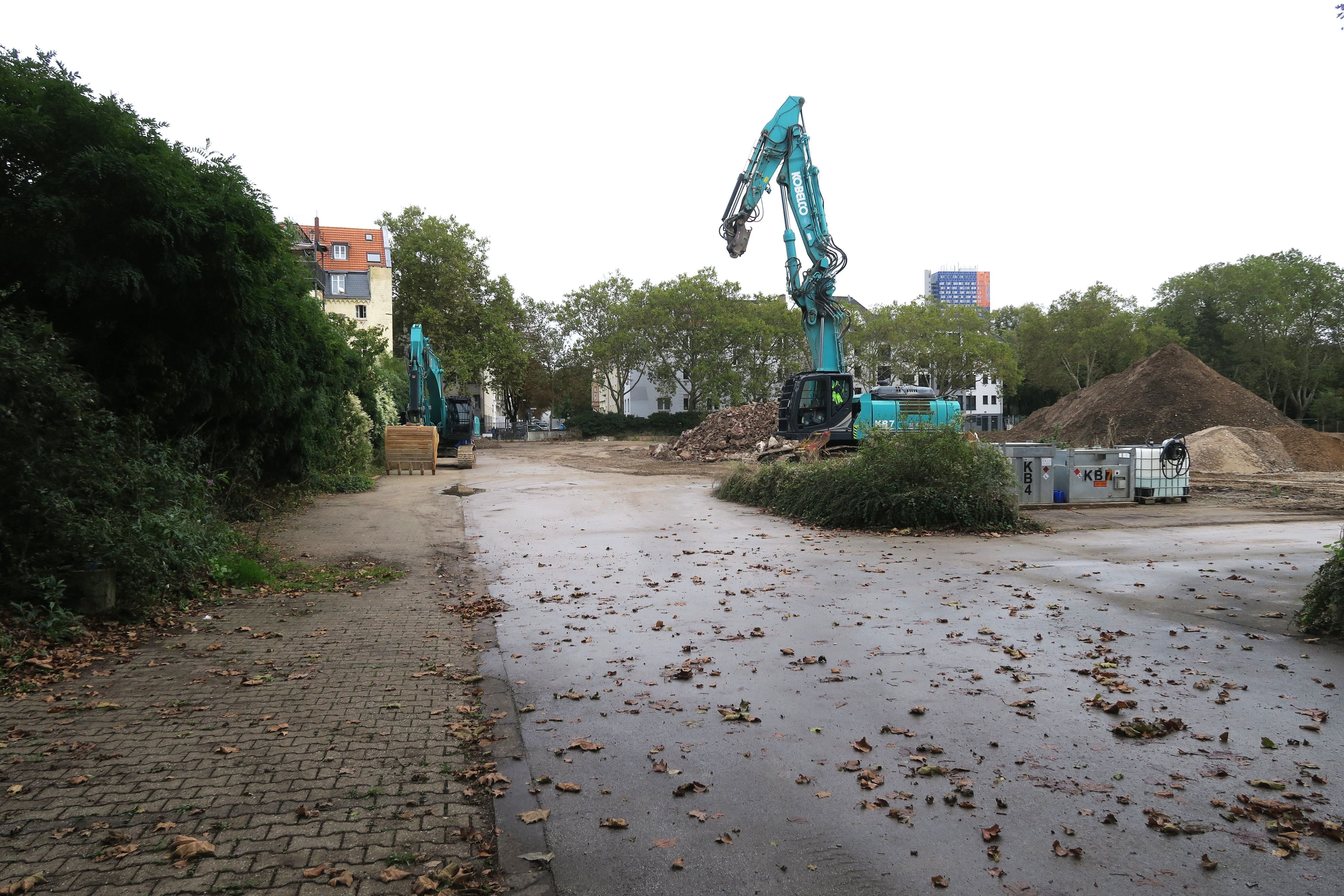 Zwei Bagger stehen auf einem Baugrundstück. Eine Straße führt seitlich daran vorbei.