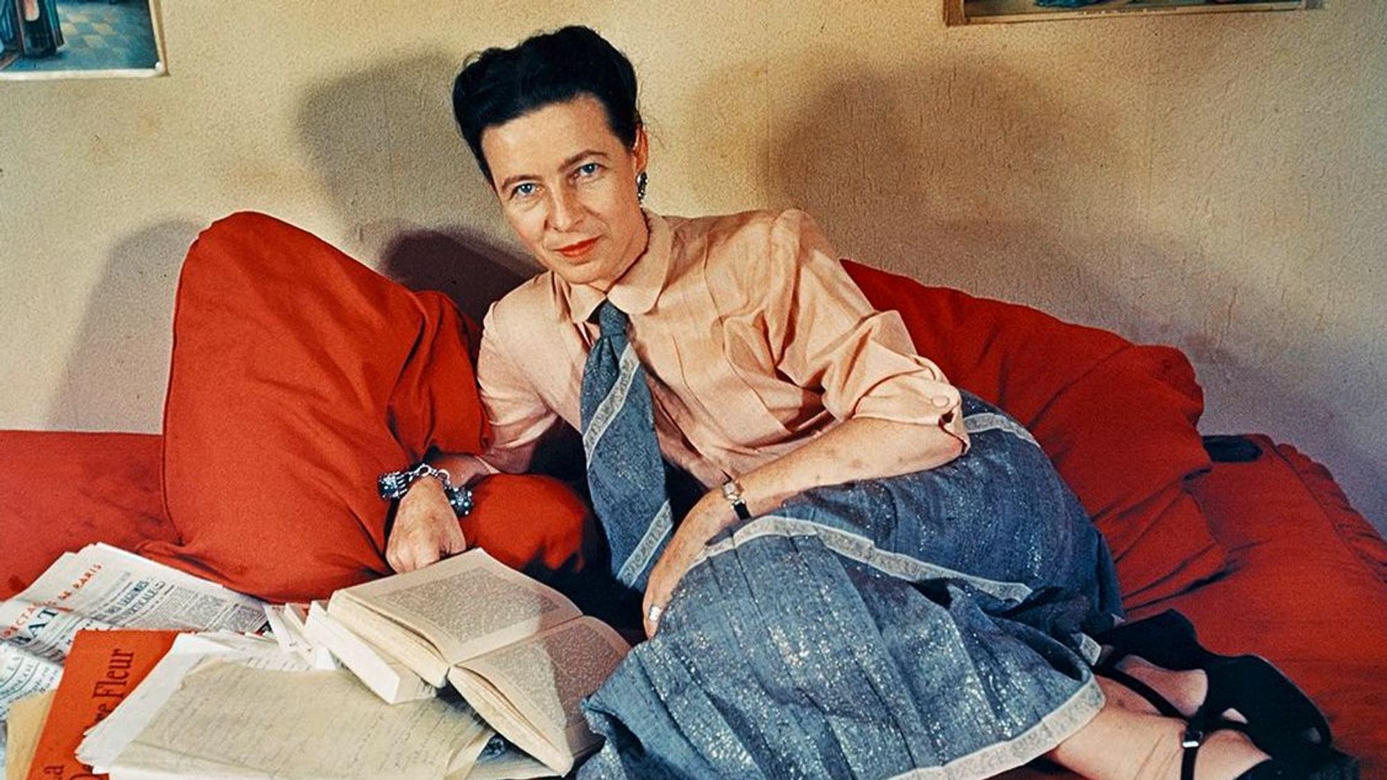 Eine Frau liegt mit Büchern auf einer roten Couch.