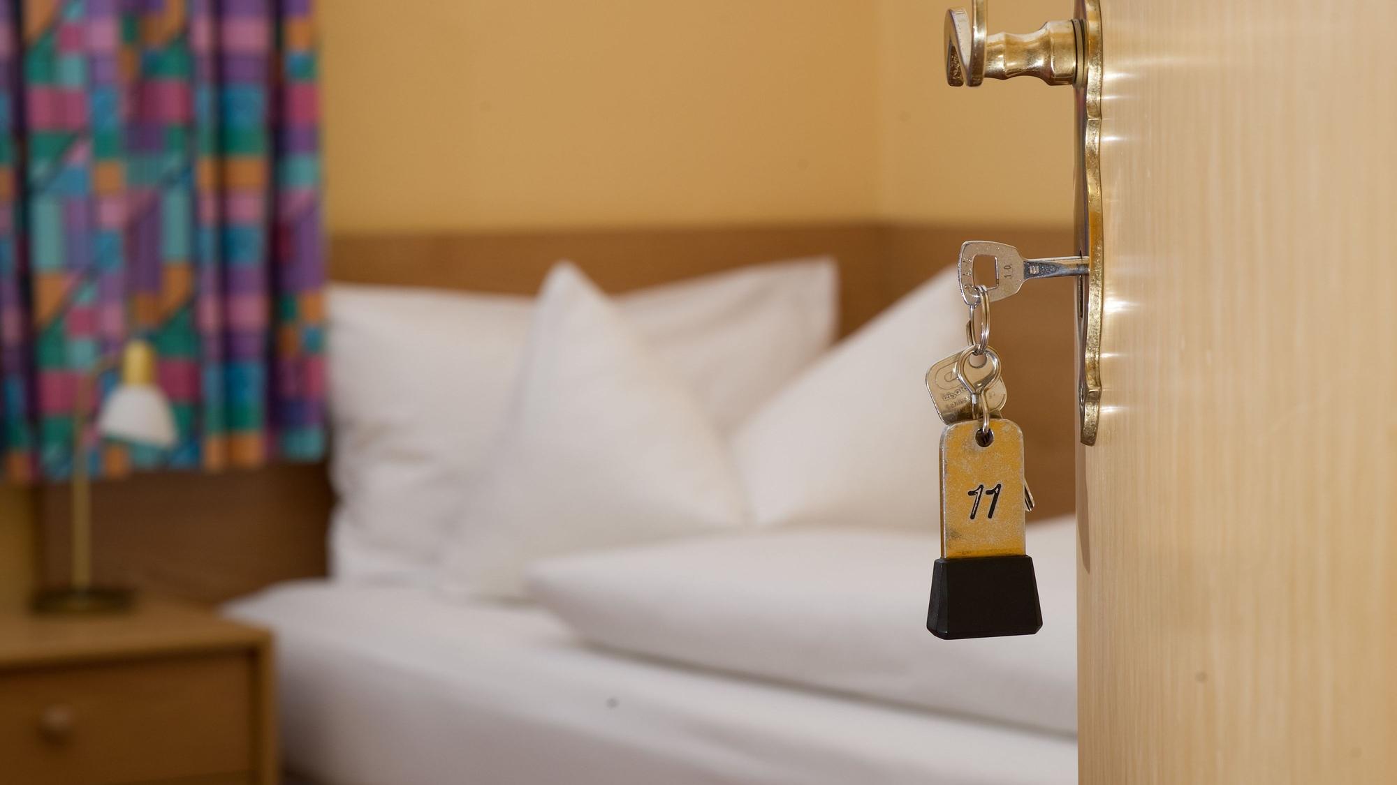 Ein Zimmerschlüssel hängt in einem Gästehaus vor einem Bett im Türschloss.