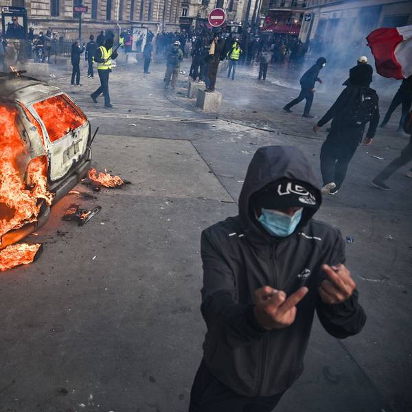 Auf dem Place de la République brennt ein Auto, davor zeigt eine vermummte Person den Mittelfinger.