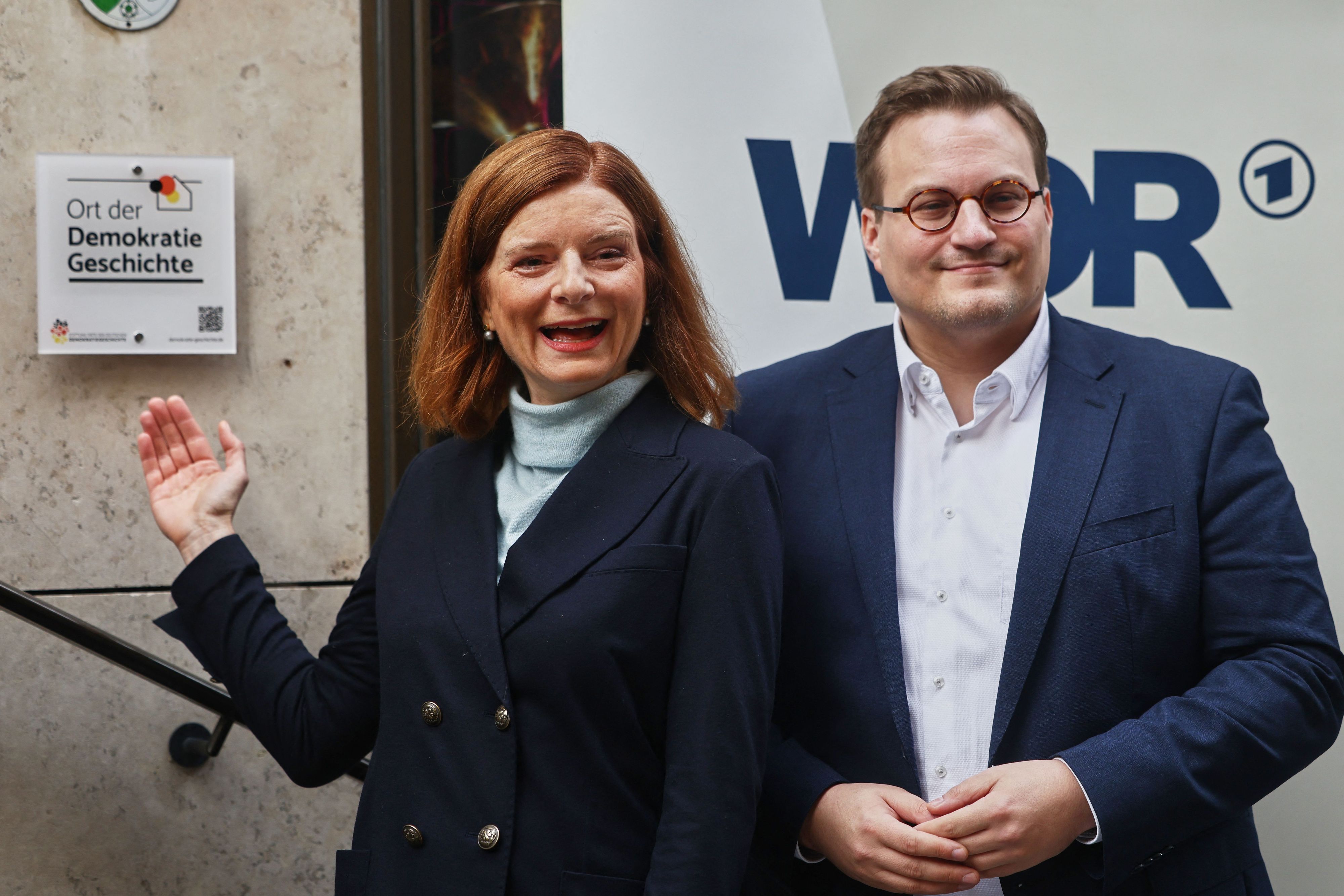 Katrin Vernau, (l.) WDR-Intendantin, steht neben Carsten Männlein, Vertreter der Stiftung „Orte der Demokratiegeschichte“, an der Plakette der Auszeichnung „Ort der Demokratiegeschichte“.