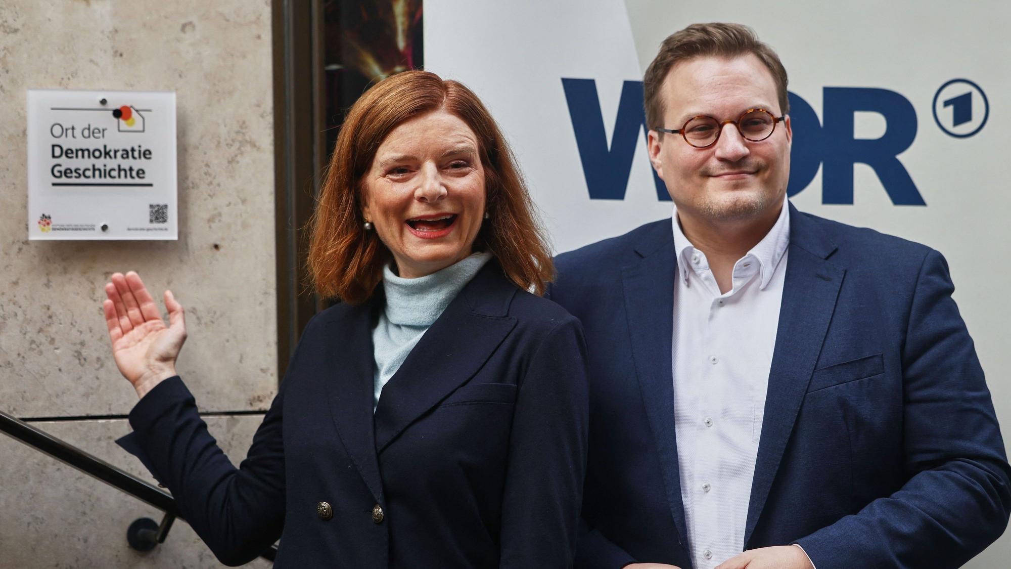 Katrin Vernau, (l.) WDR-Intendantin, steht neben Carsten Männlein, Vertreter der Stiftung „Orte der Demokratiegeschichte“, an der Plakette der Auszeichnung „Ort der Demokratiegeschichte“.