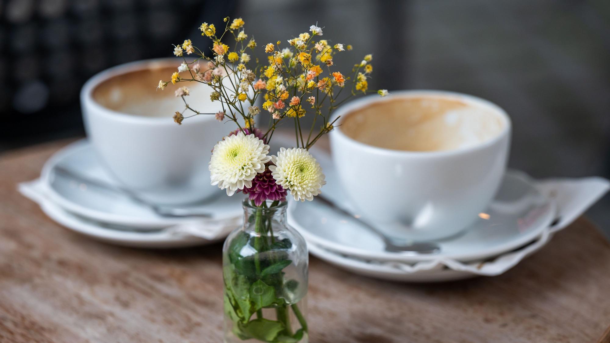 ARCHIV - 16.08.2021, Bayern, München: Eine kleine Vase mit Blumen steht in einem Straßencafe in der Innenstadt auf einem Tisch vor zwei benutzten, leeren Kaffeetassen. (zu dpa: «Sporadisch Café-Small-Talk: Sind wir nur noch Pseudofreunde?») Foto: Peter Kneffel/dpa +++ dpa-Bildfunk +++