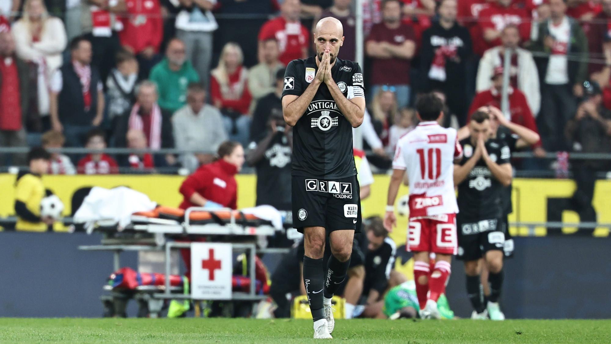 Ein Spieler von Sturm Graz zeigt sich schockiert von der Verletzung seines Teamkollegen Daniil Khudyakov, der im Hintergrund behandelt wird.