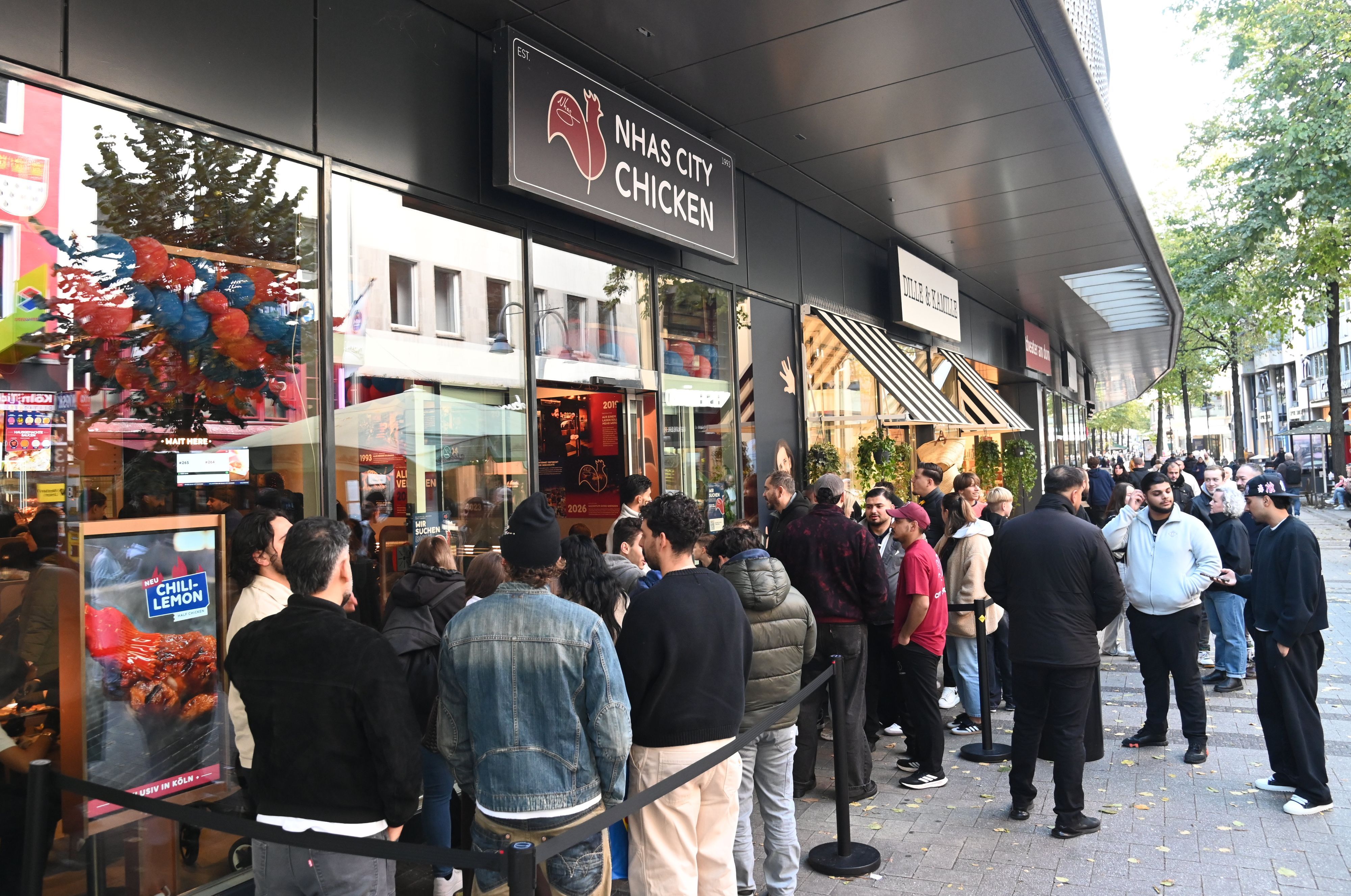 Menschen stehen vor dem Fast-Food-Imbiss Nhas City Chicken an der Breite Straße.